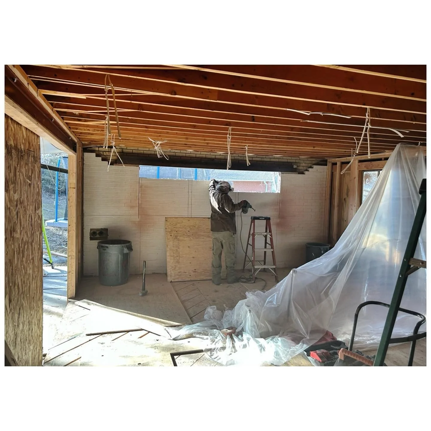 Renovation space with exposed timber roof framing and protective sheets over furnishings