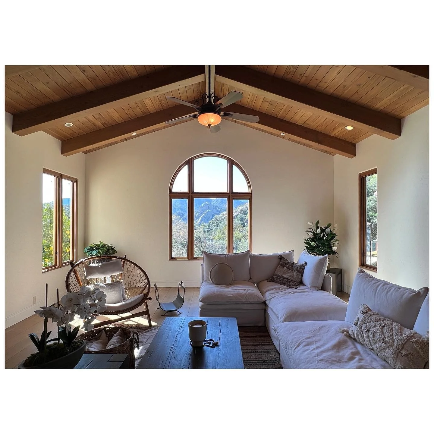 Living room beneath a pitched timber ceiling with an arched window and pale sofa