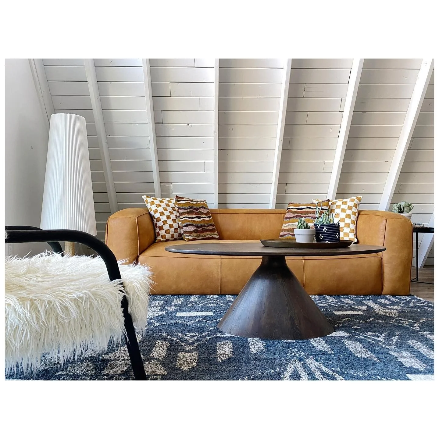 Mustard-colored sofa beneath white A-frame roof beams beside a black lounge chair