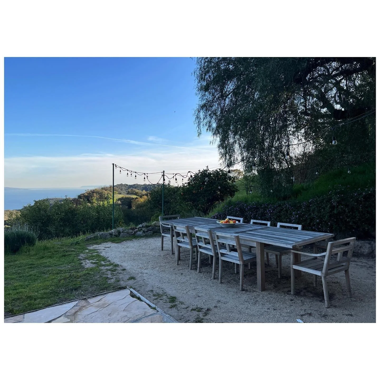 Long outdoor dining table with white chairs overlooking a wooded canyon