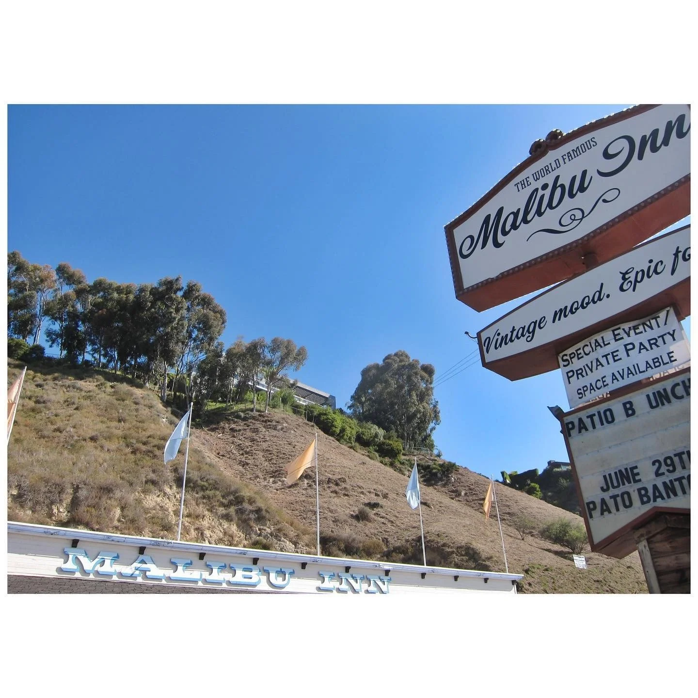 Malibu Inn roadside sign beside a sunlit hillside