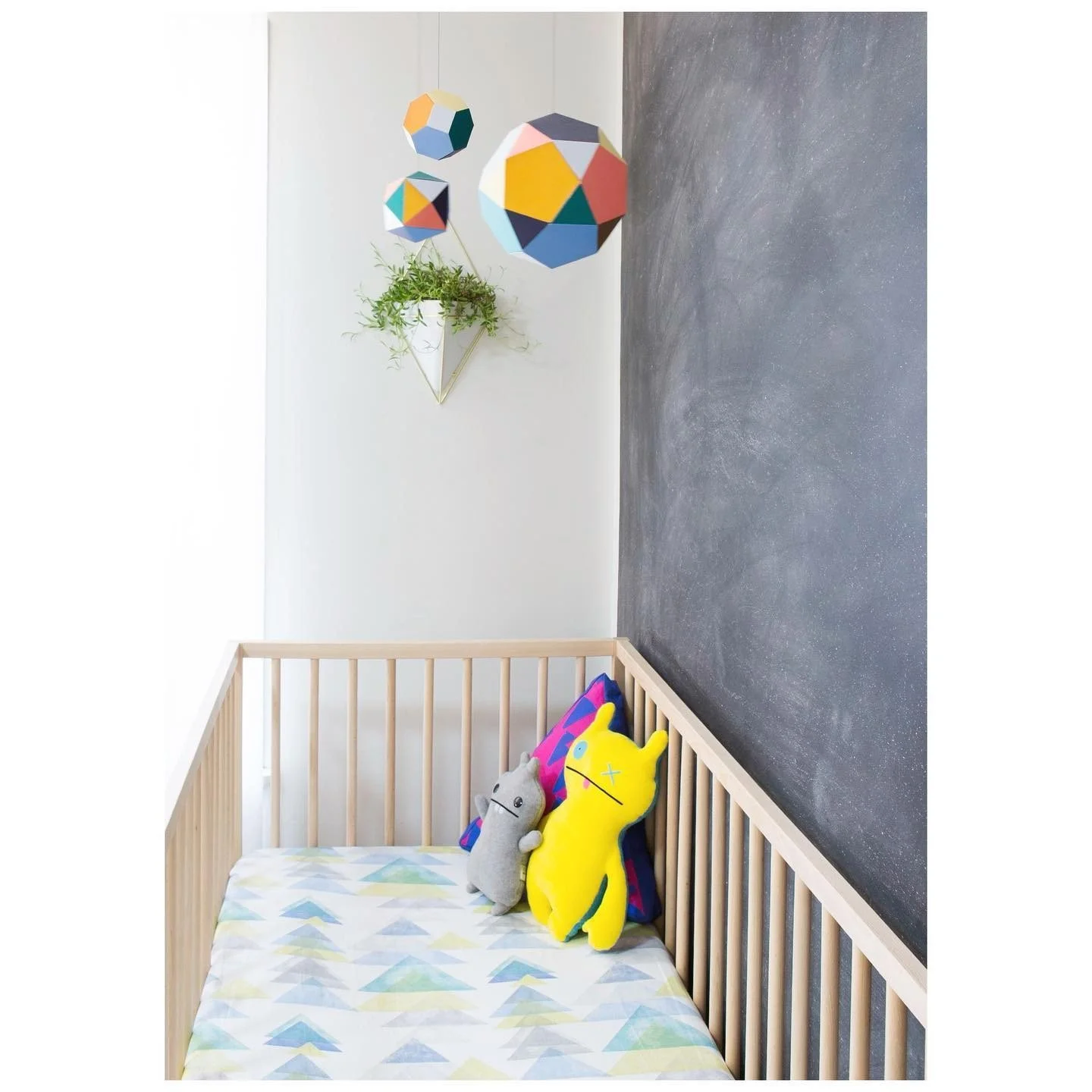 Pale timber crib beneath a colorful mobile beside a dark gray accent wall