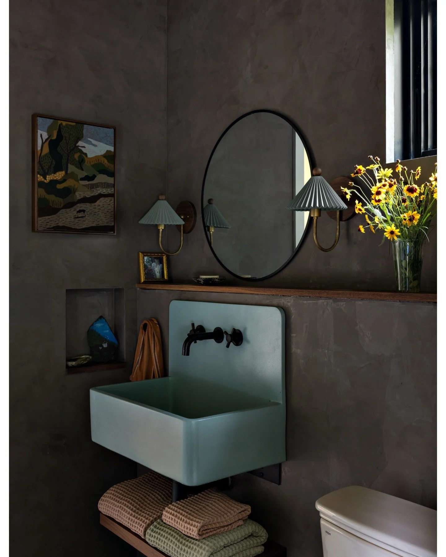 Sculptural pale green basin beneath an oval mirror and dark plum walls