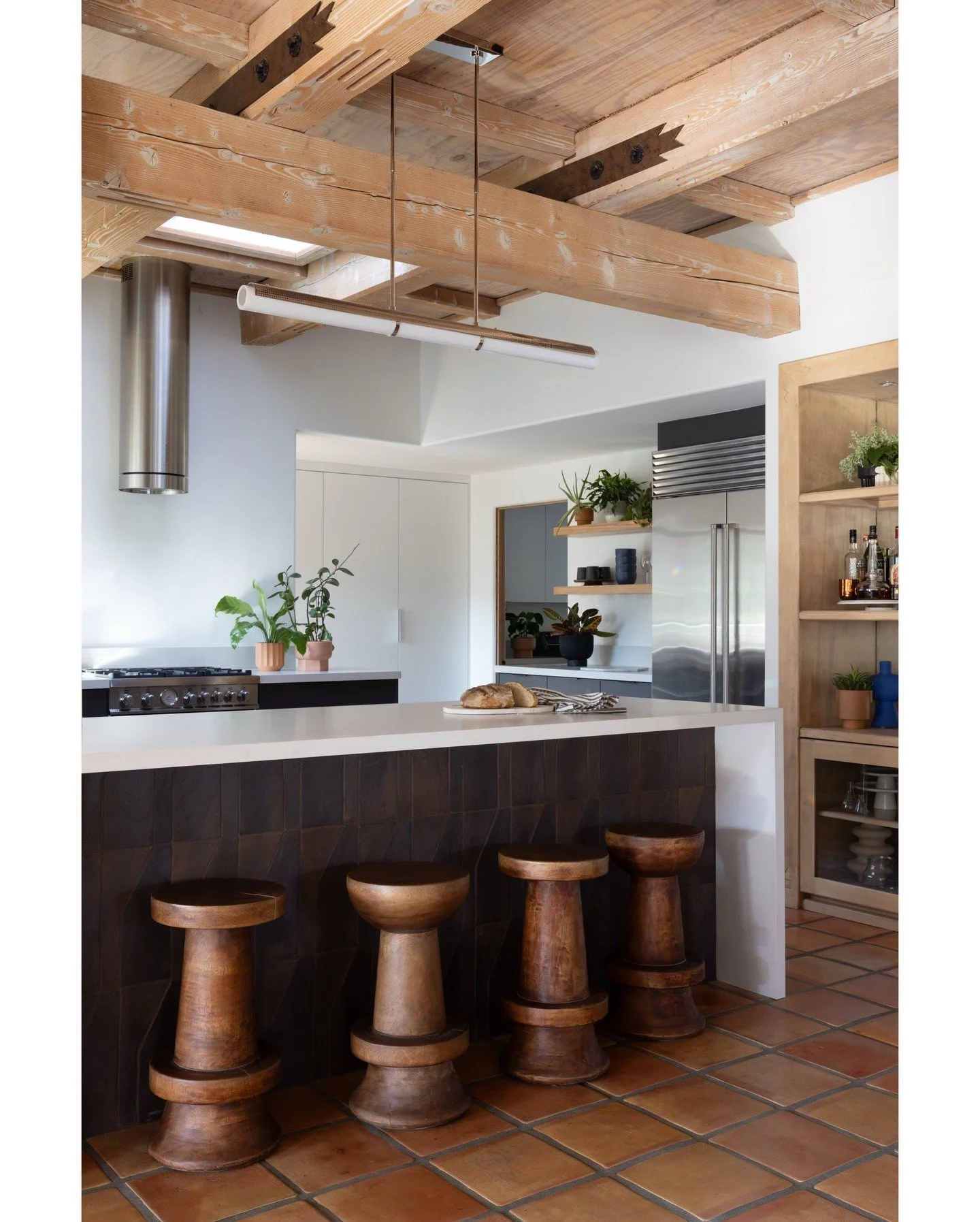Kitchen island with dark timber stools beneath an exposed timber ceiling