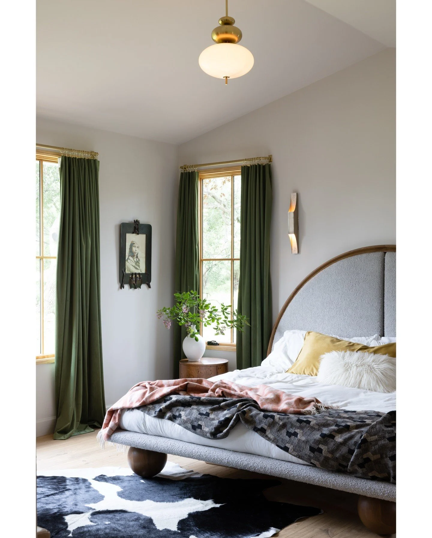 Bedroom with an arched timber bed layered patterned bedding and green curtains
