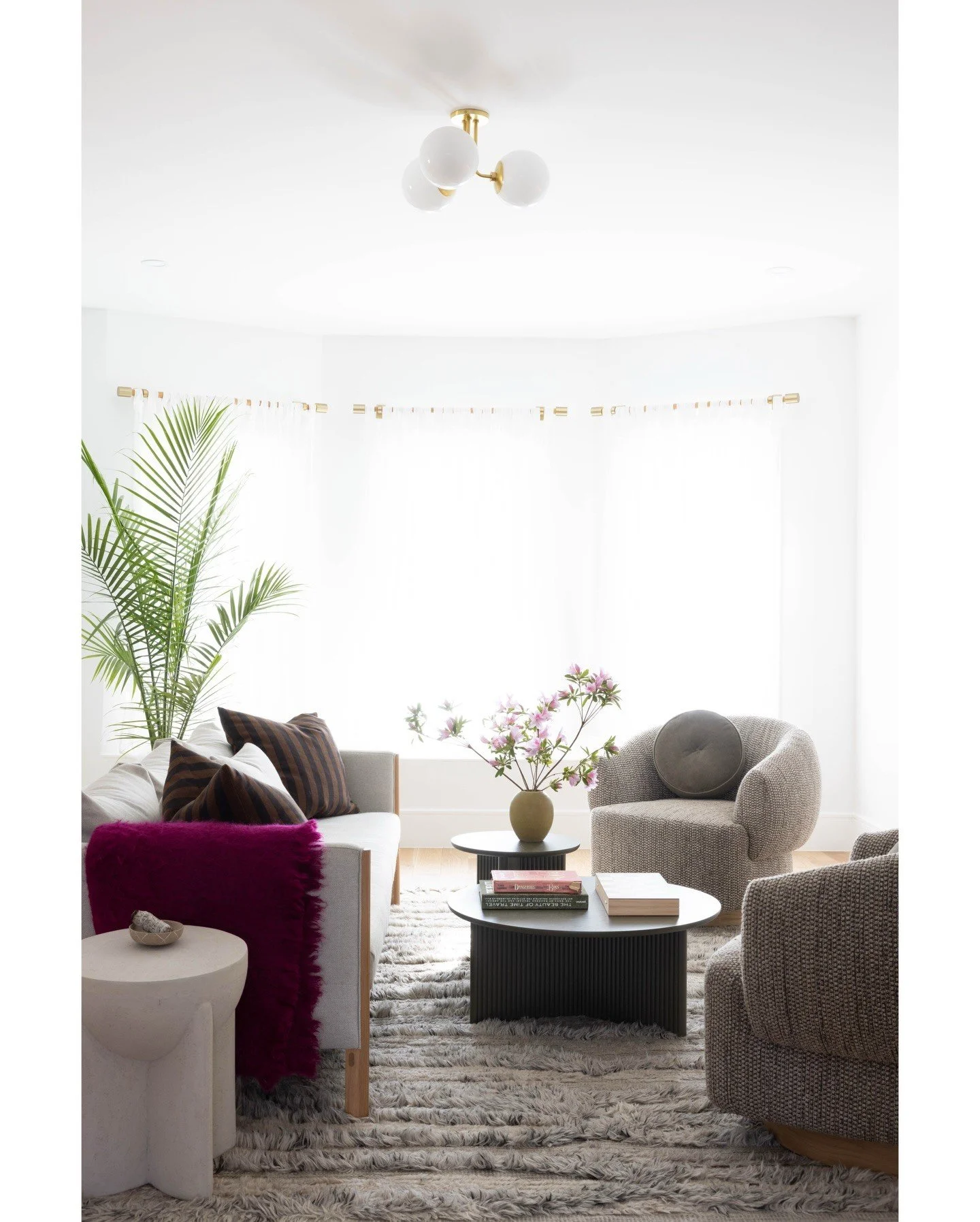 Sunlit living room with pale seating plants and a dark purple upholstered stool