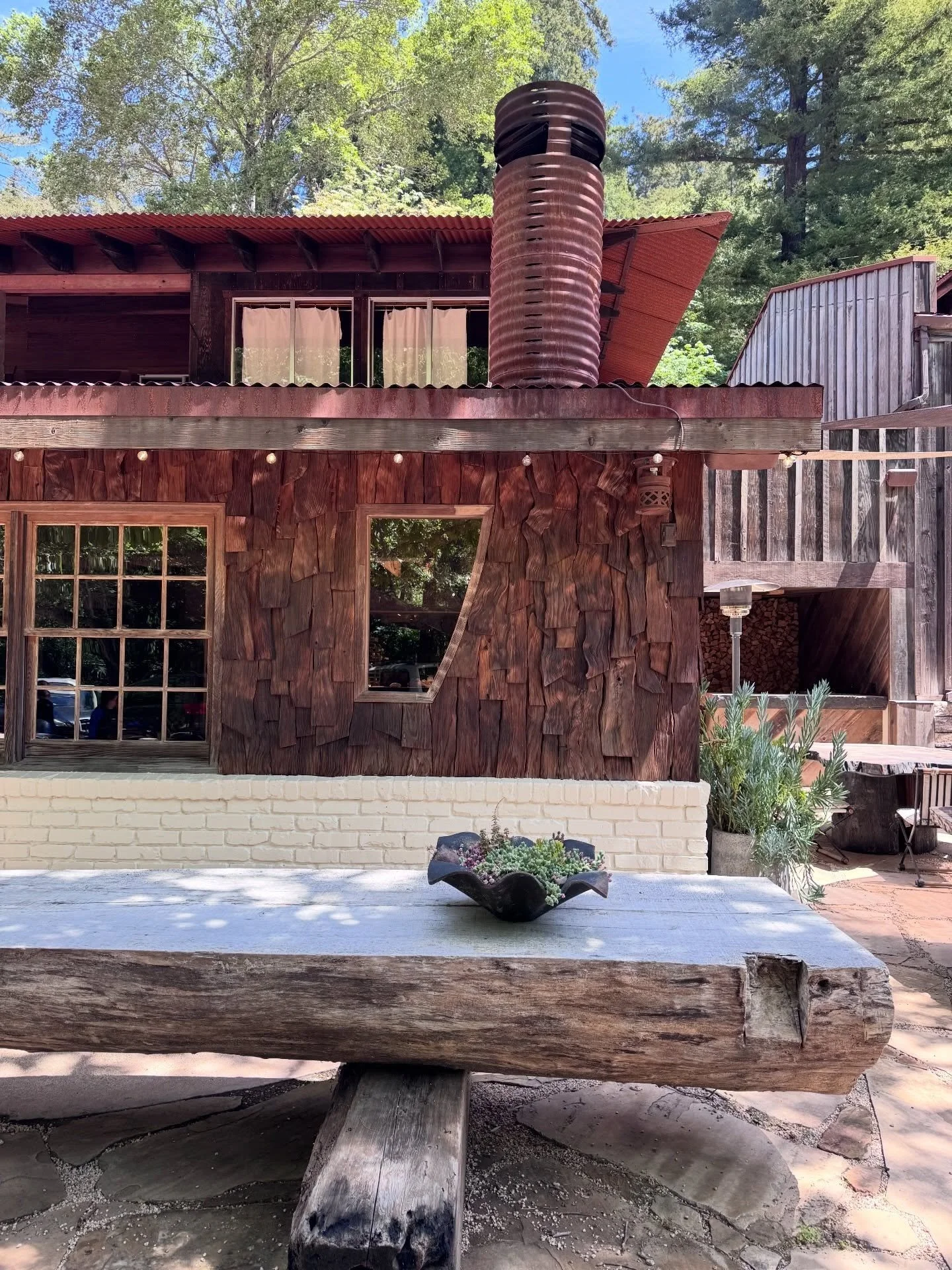 Rustic timber building with a red metal chimney beside outdoor dining tables