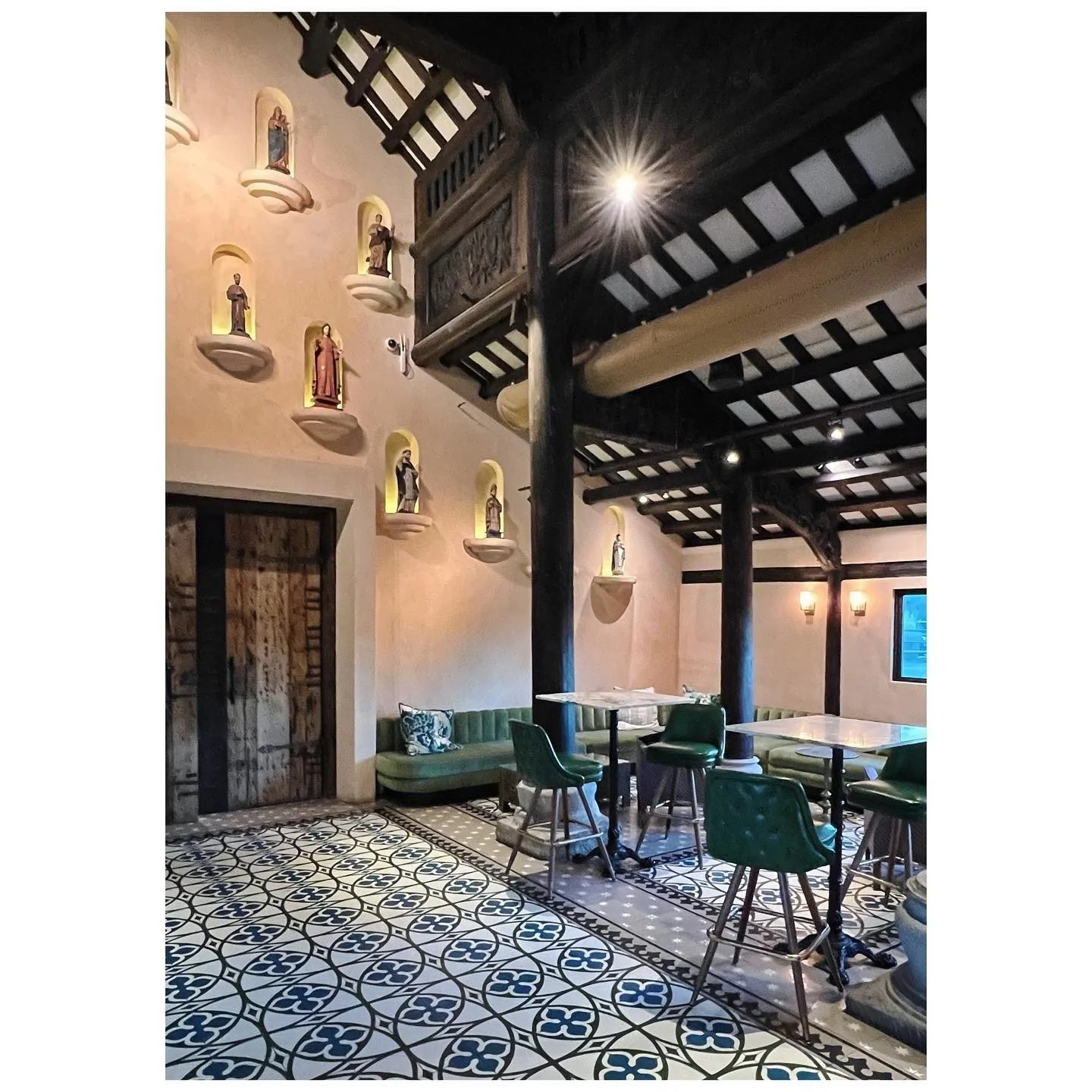 Double-height restaurant courtyard with patterned floors, green seating and dark timber balconies