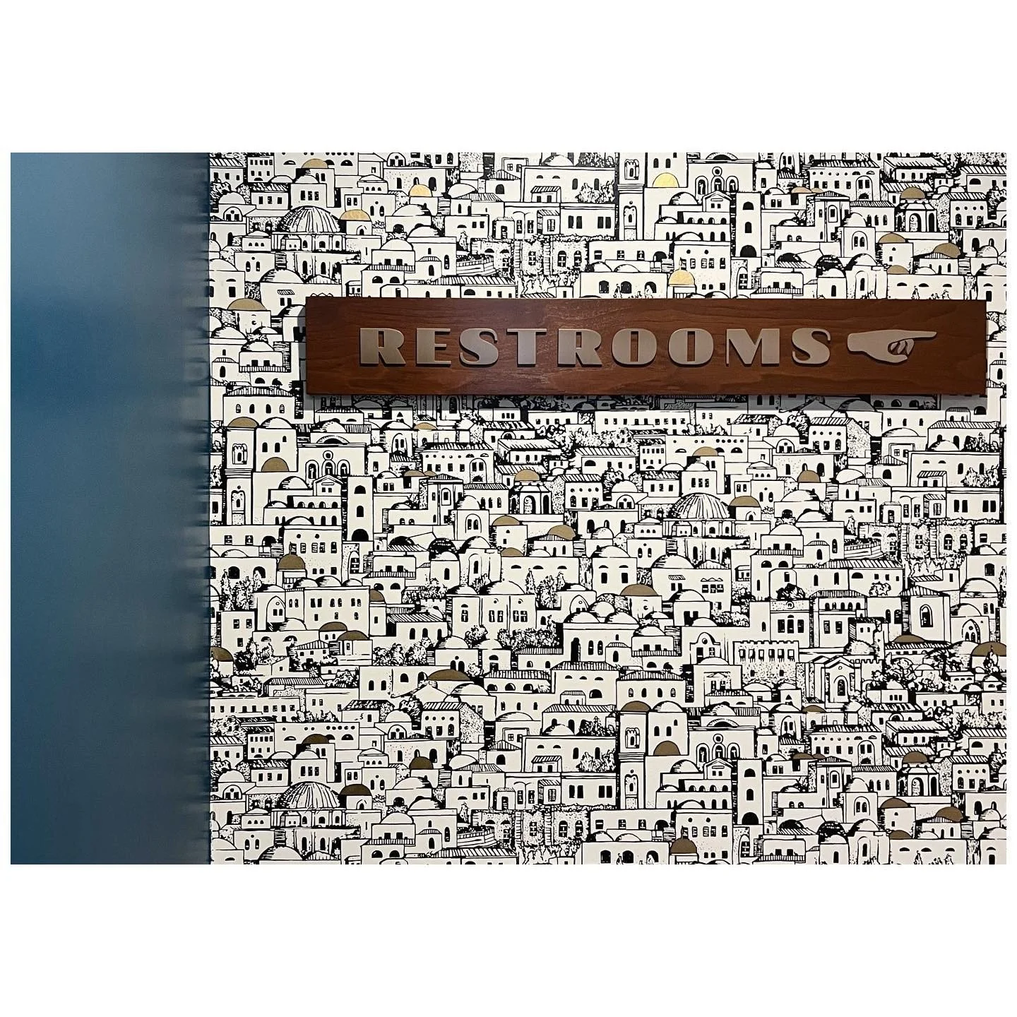 Black-and-white illustrated building wallpaper around a timber restroom sign