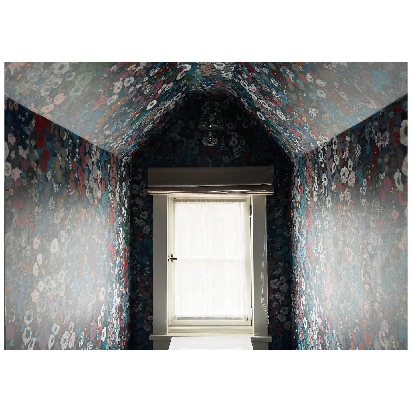 Floral wallpaper covers the walls and sloping ceiling around a tall window