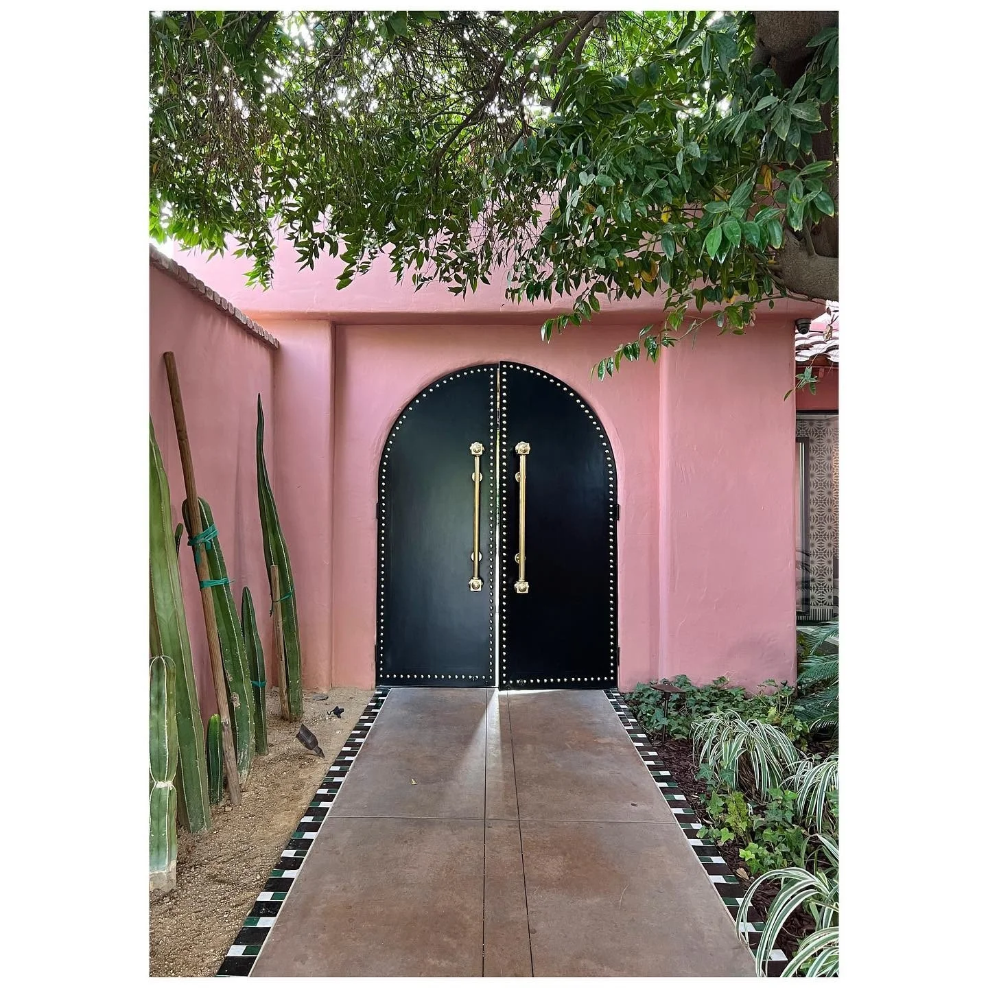 Pink courtyard walls frame an arched dark doorway, tiled path and desert planting
