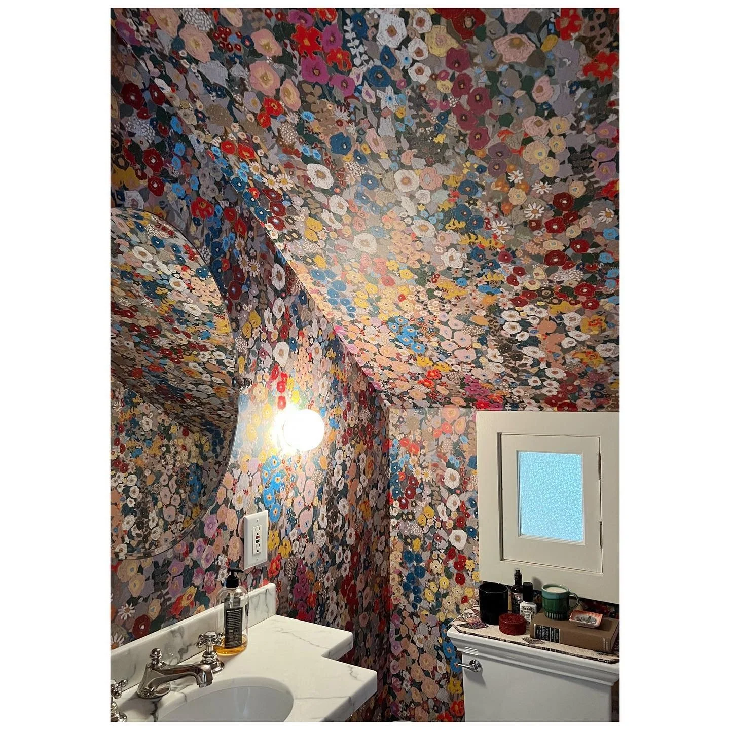 Colorful floral wallpaper extends across the bathroom ceiling above a curved mirror and white basin