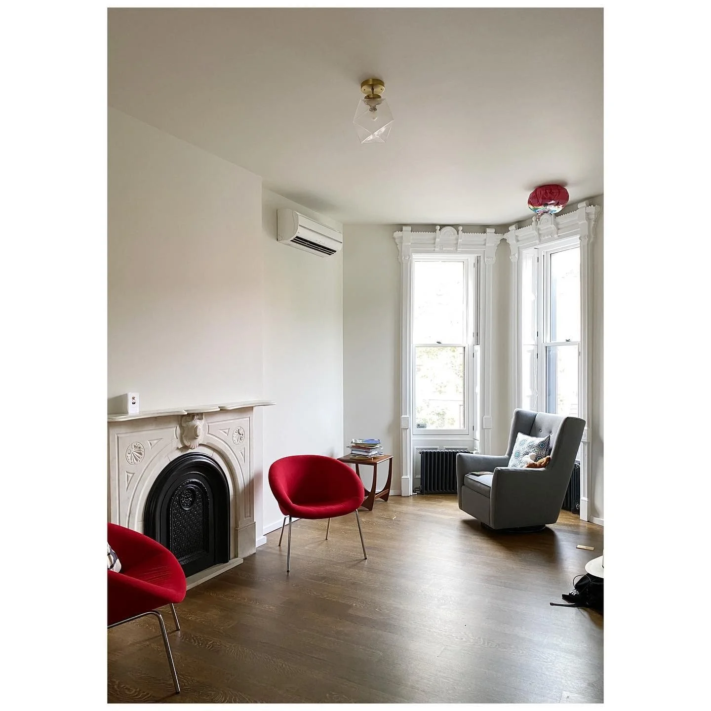 Parlor before wallpaper with pale walls, a black fireplace and red and gray chairs