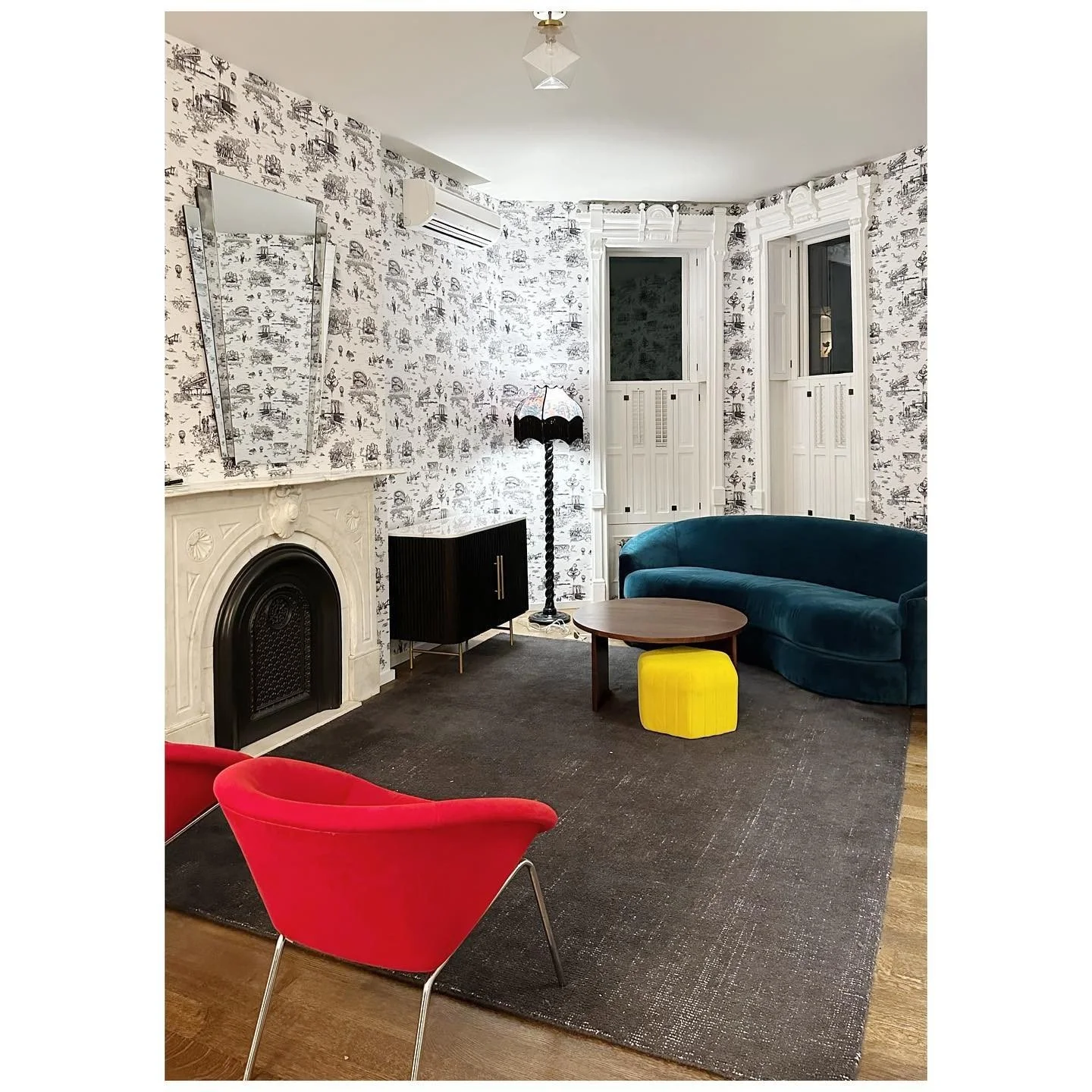 Wallpapered parlor with a white period fireplace, red lounge chair and curved teal sofa
