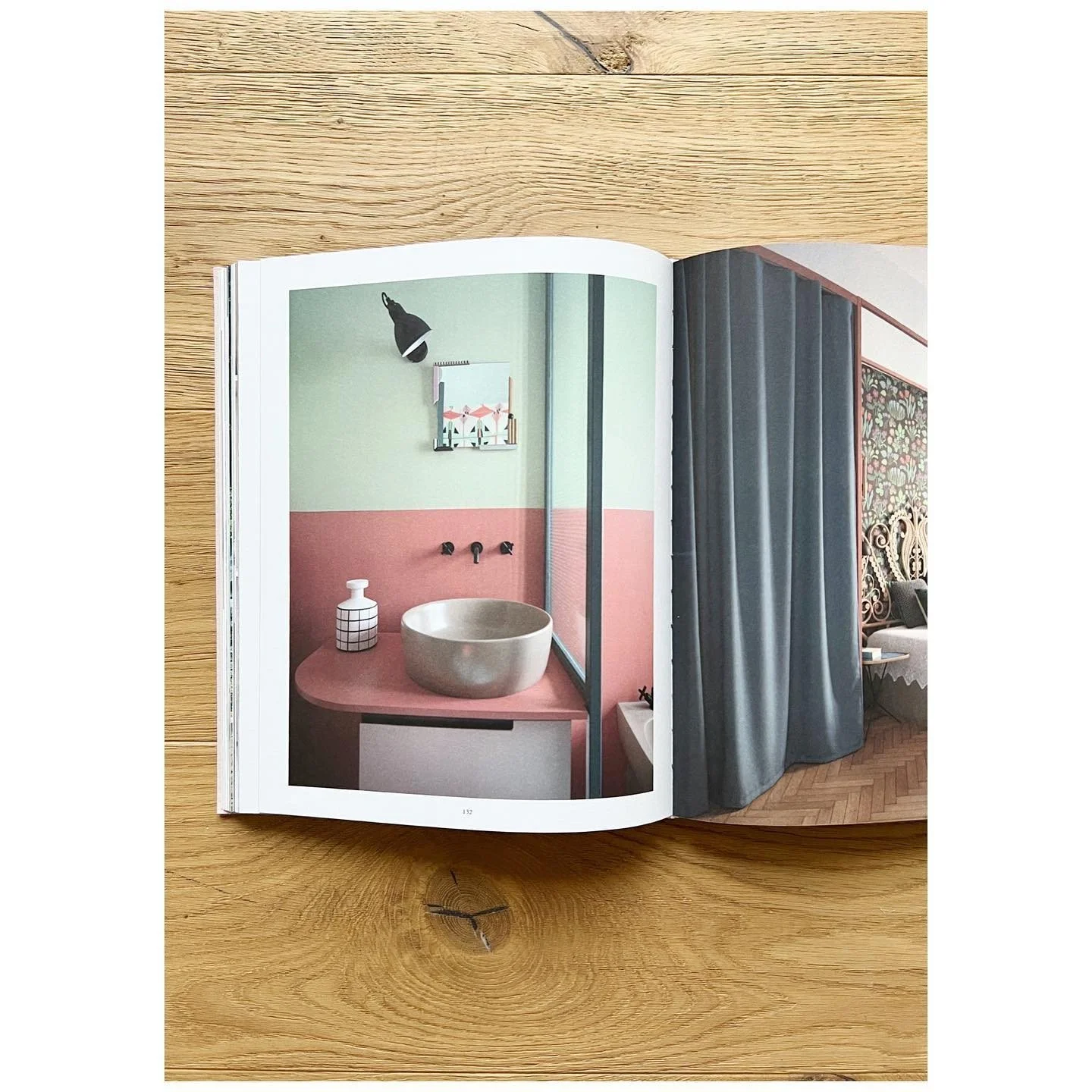 Open design book on a timber floor showing a bathroom with pink and green walls and a metal basin
