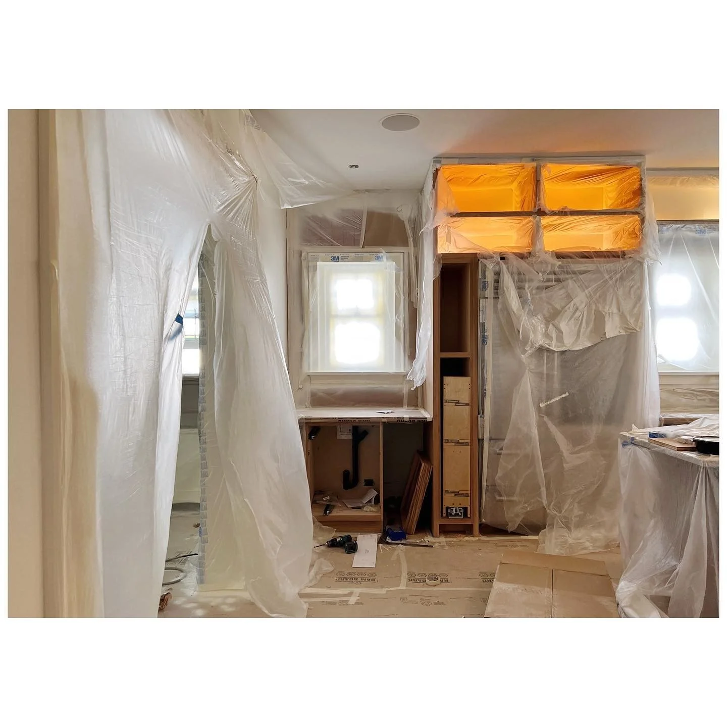 Kitchen installation protected with plastic sheeting around newly fitted cabinets and a window