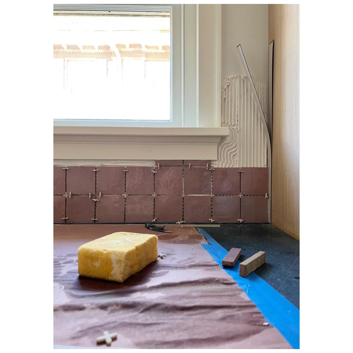 Handmade pale pink tiles being installed below a kitchen window