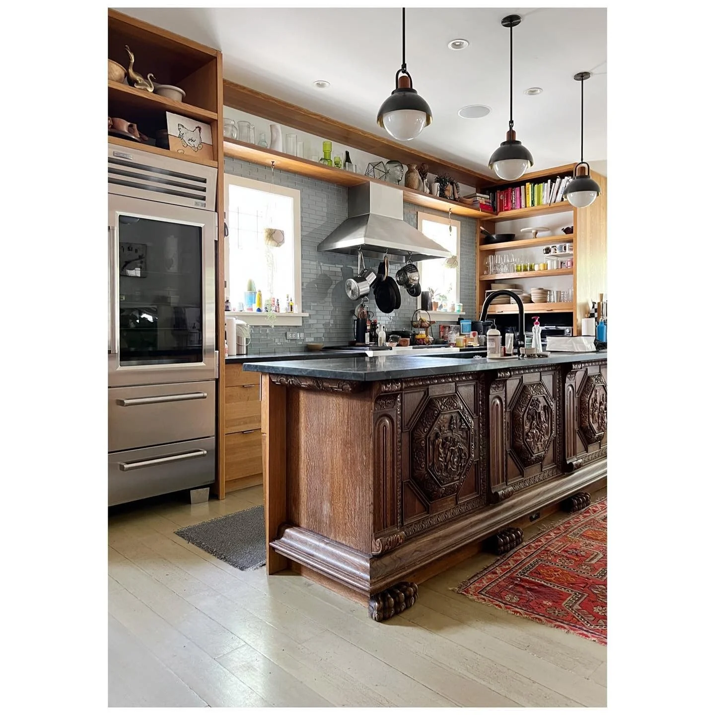 Close view of carved timber island panels, dark countertops and open kitchen shelves