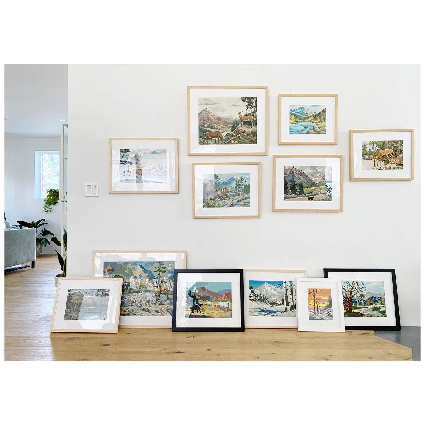 Framed vintage landscape paintings arranged on a pale wall with additional pictures ready below