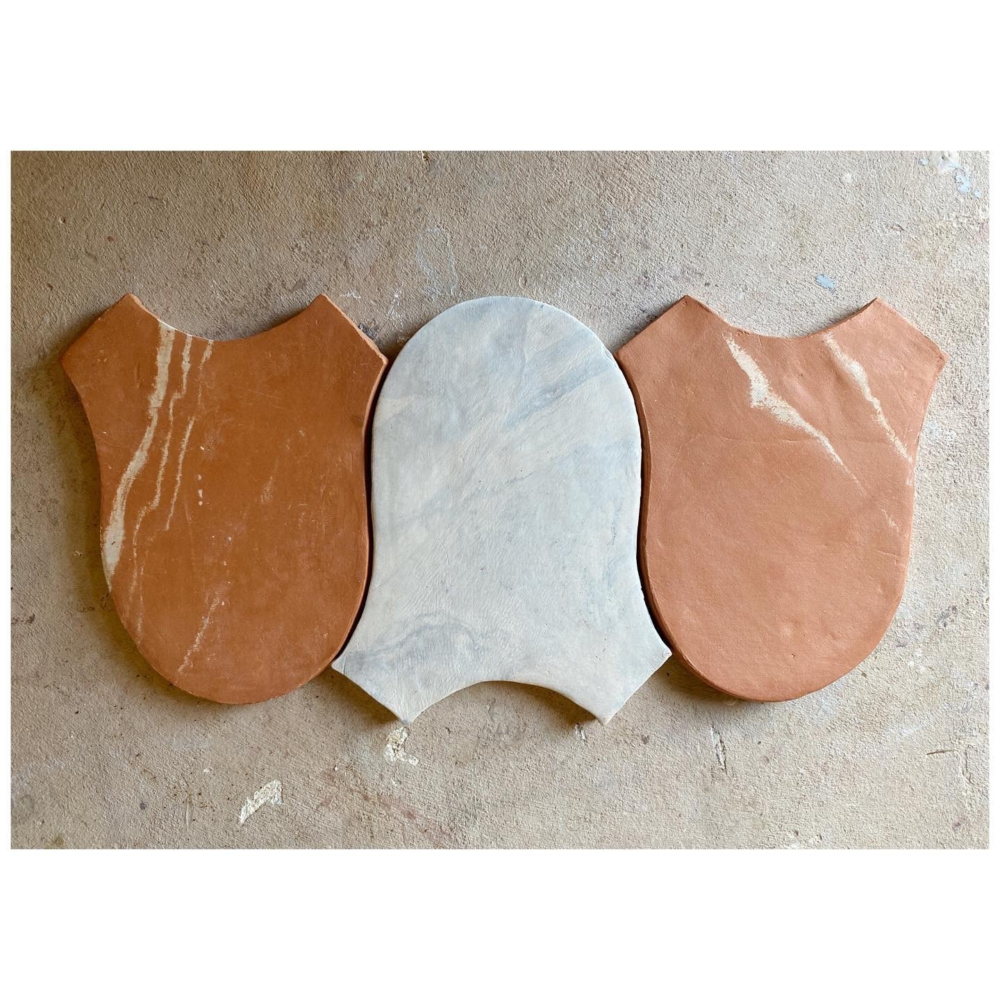 Three handmade interlocking clay tiles in rust, pale blue and warm pink