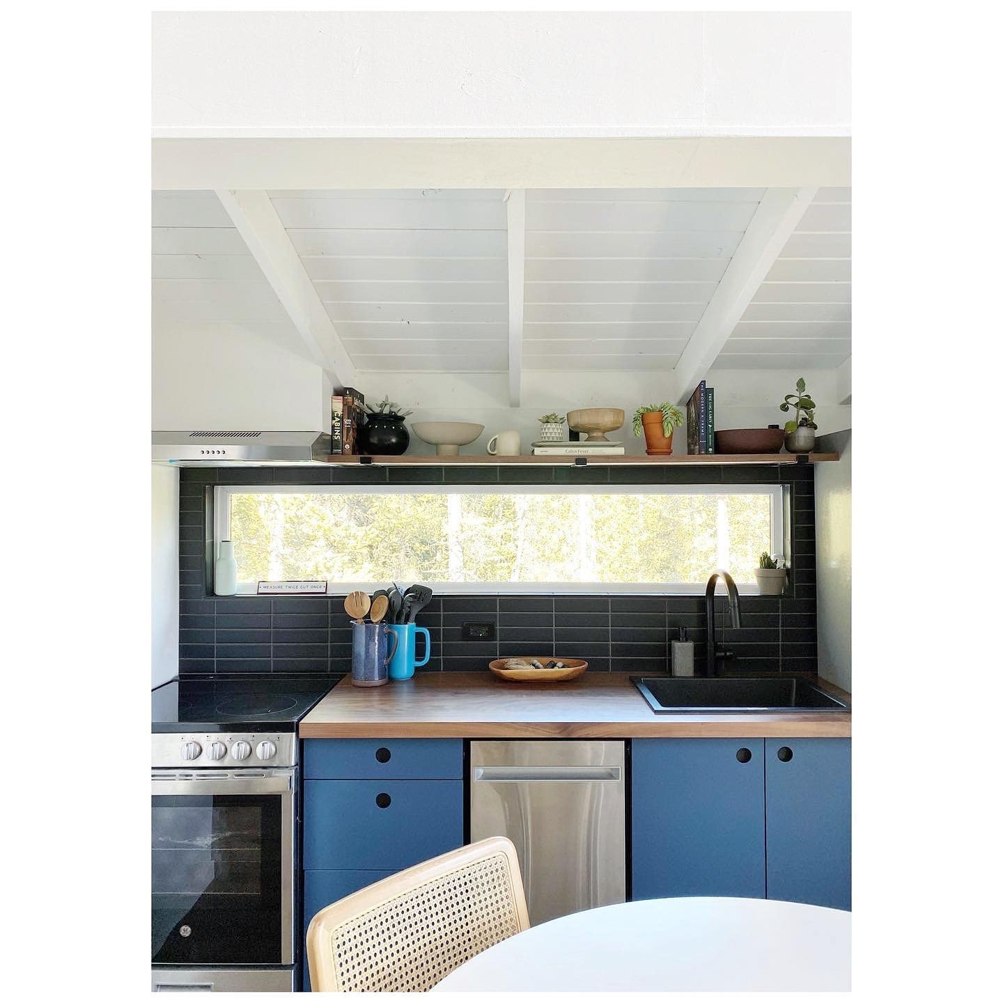 Refreshed cabin kitchen with blue cabinets, a dark tile backsplash, timber countertop and white roof beams