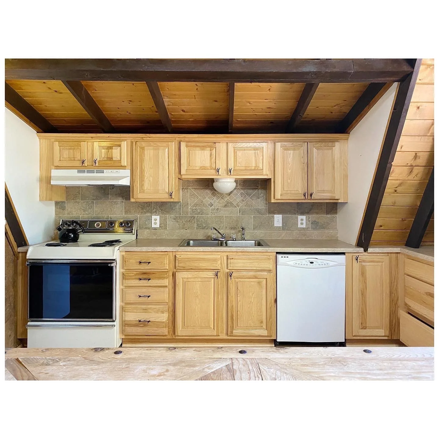 Cabin kitchen before renovation with pale timber cabinets and an unpainted ceiling
