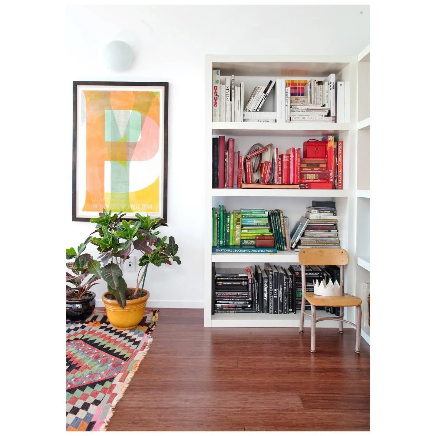 White built-in shelves arranged with colorful books beside a graphic print, timber chair and patterned rug