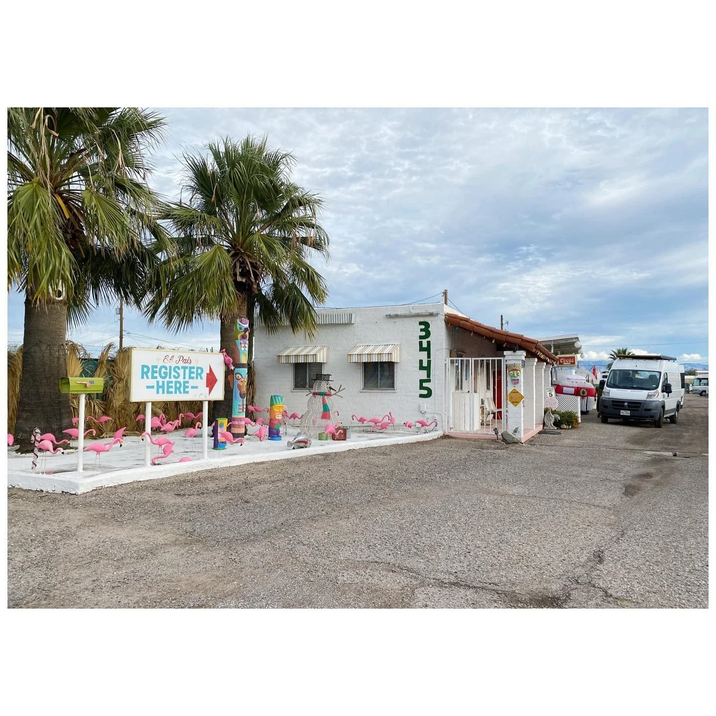 Low roadside motel office with palm trees, pink flamingo ornaments and a register-here sign