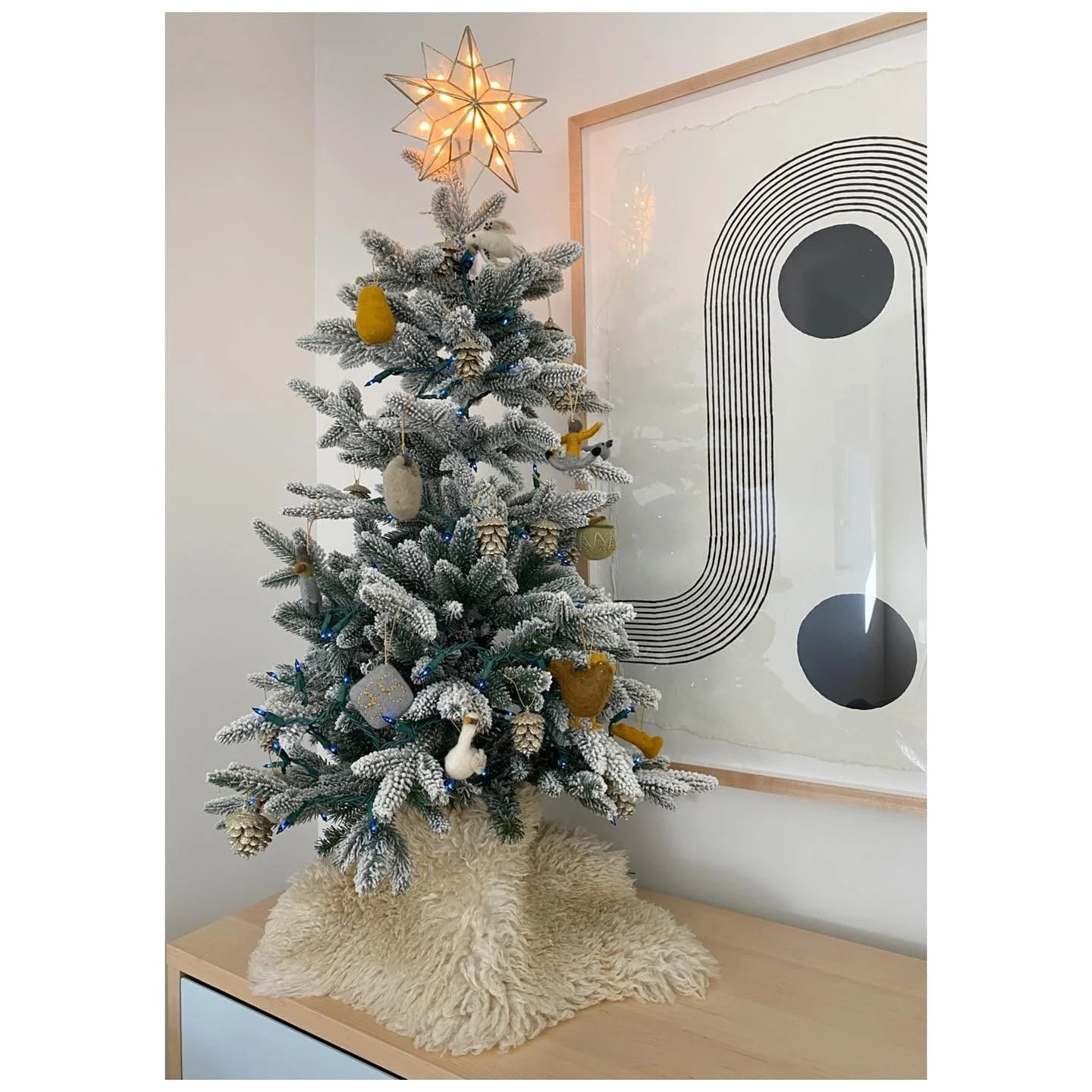 Small decorated Christmas tree with a star topper on a timber dresser beside a graphic print