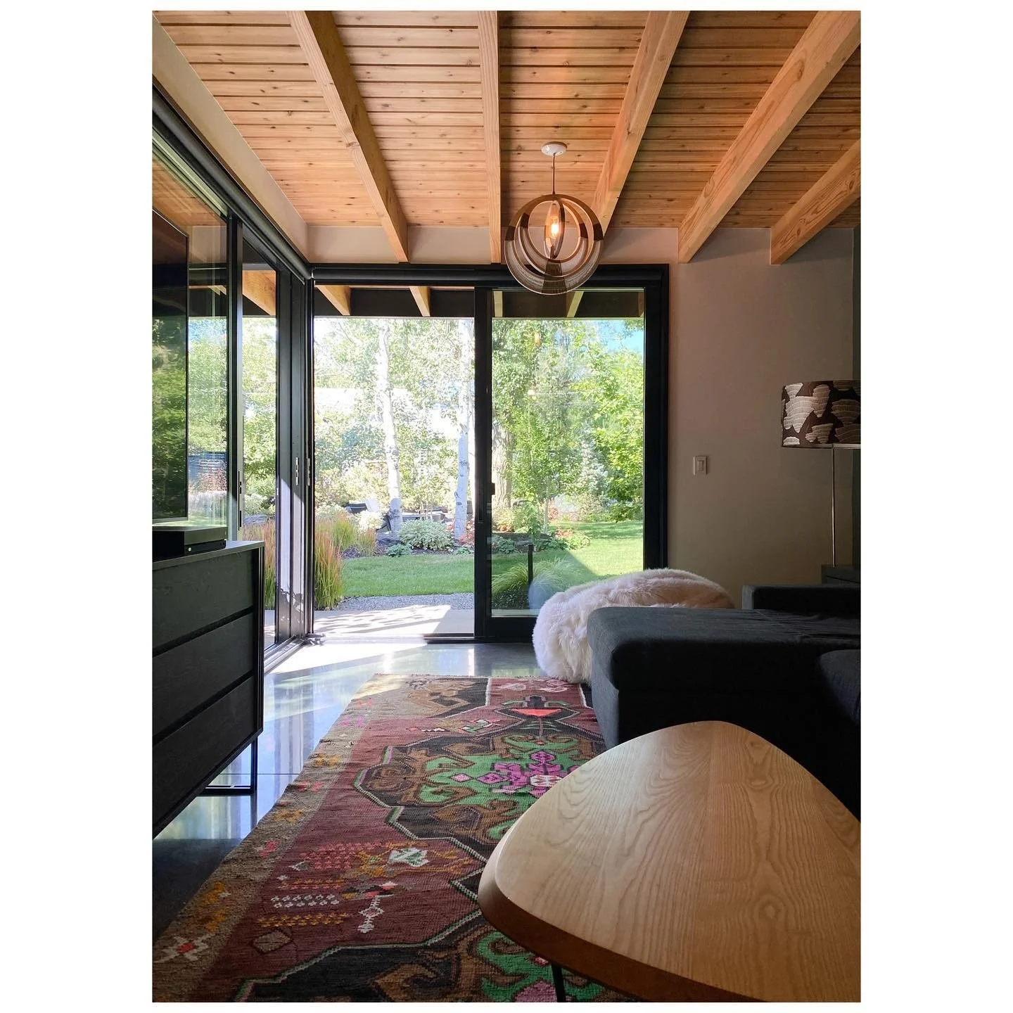 Timber-ceilinged sitting room with broad black-framed doors opening to a garden