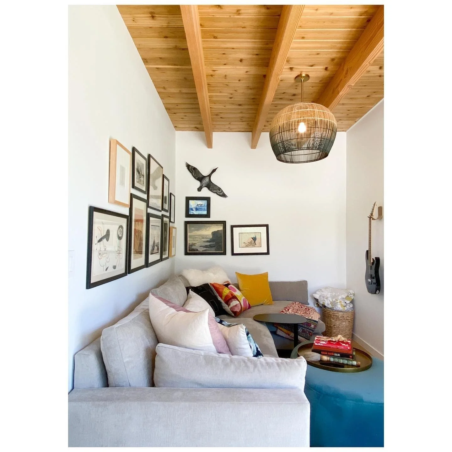 Layered living room with pale seating, a gallery wall, timber roof beams and a large woven pendant