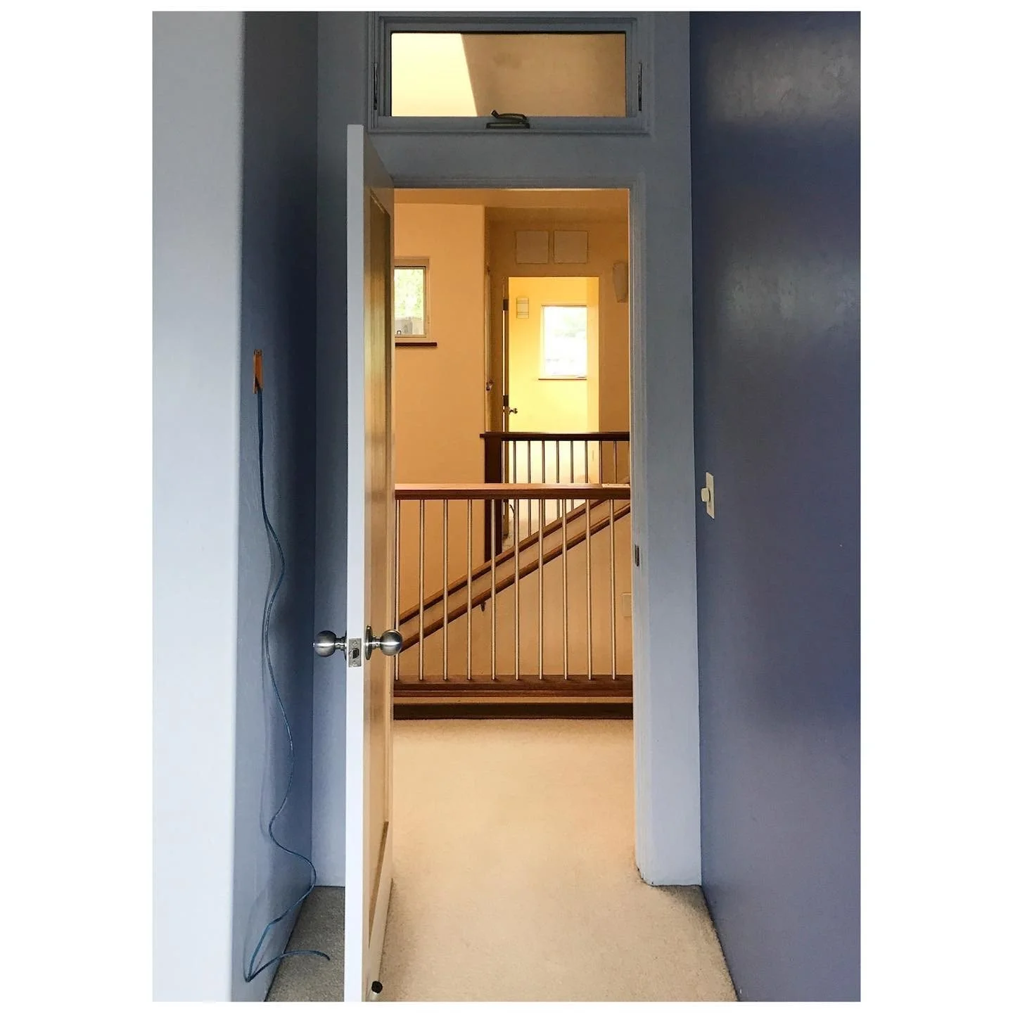 Landing before renovation seen through a narrow doorway with blue walls and carpet
