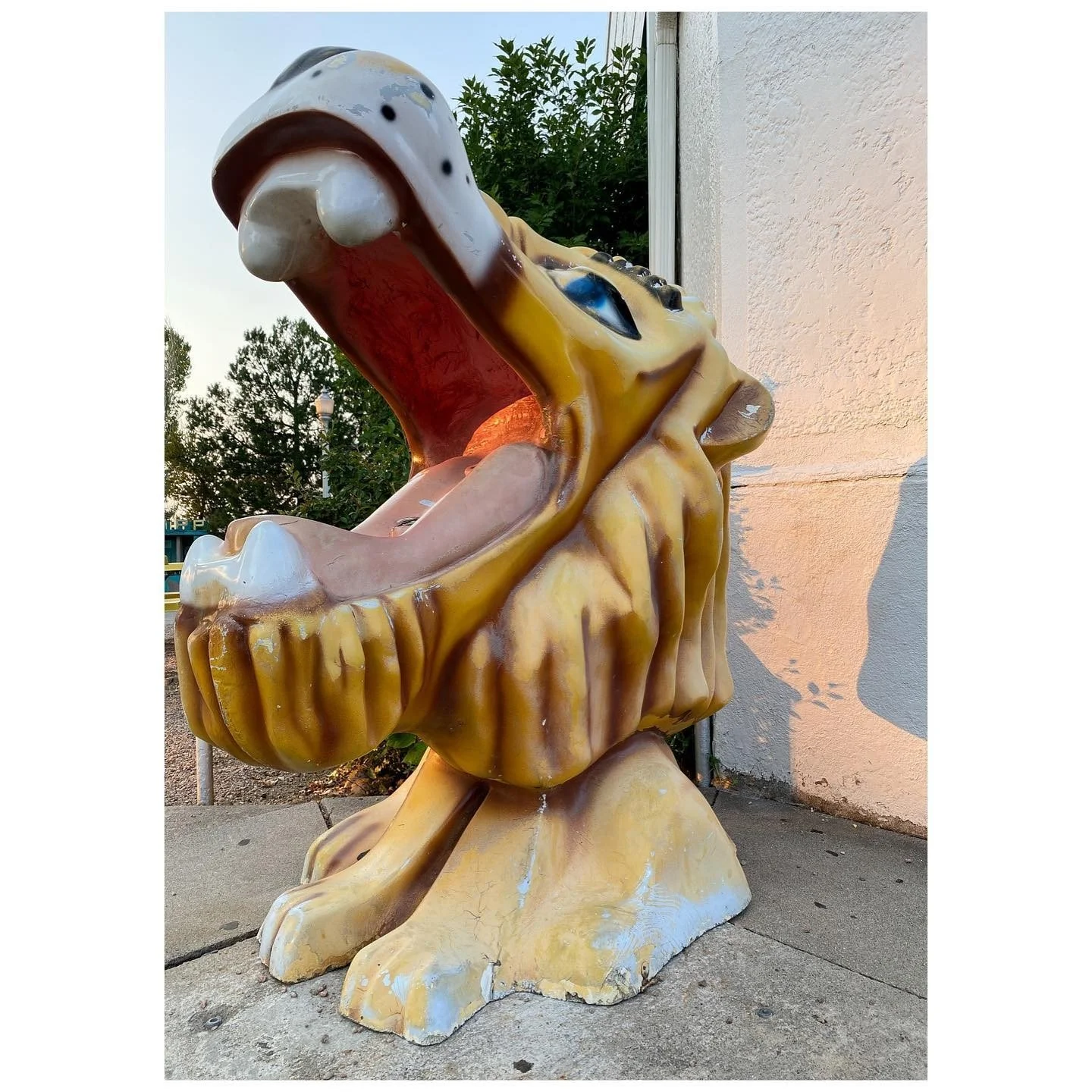 Painted yellow lion sculpture with a large open mouth at an amusement park