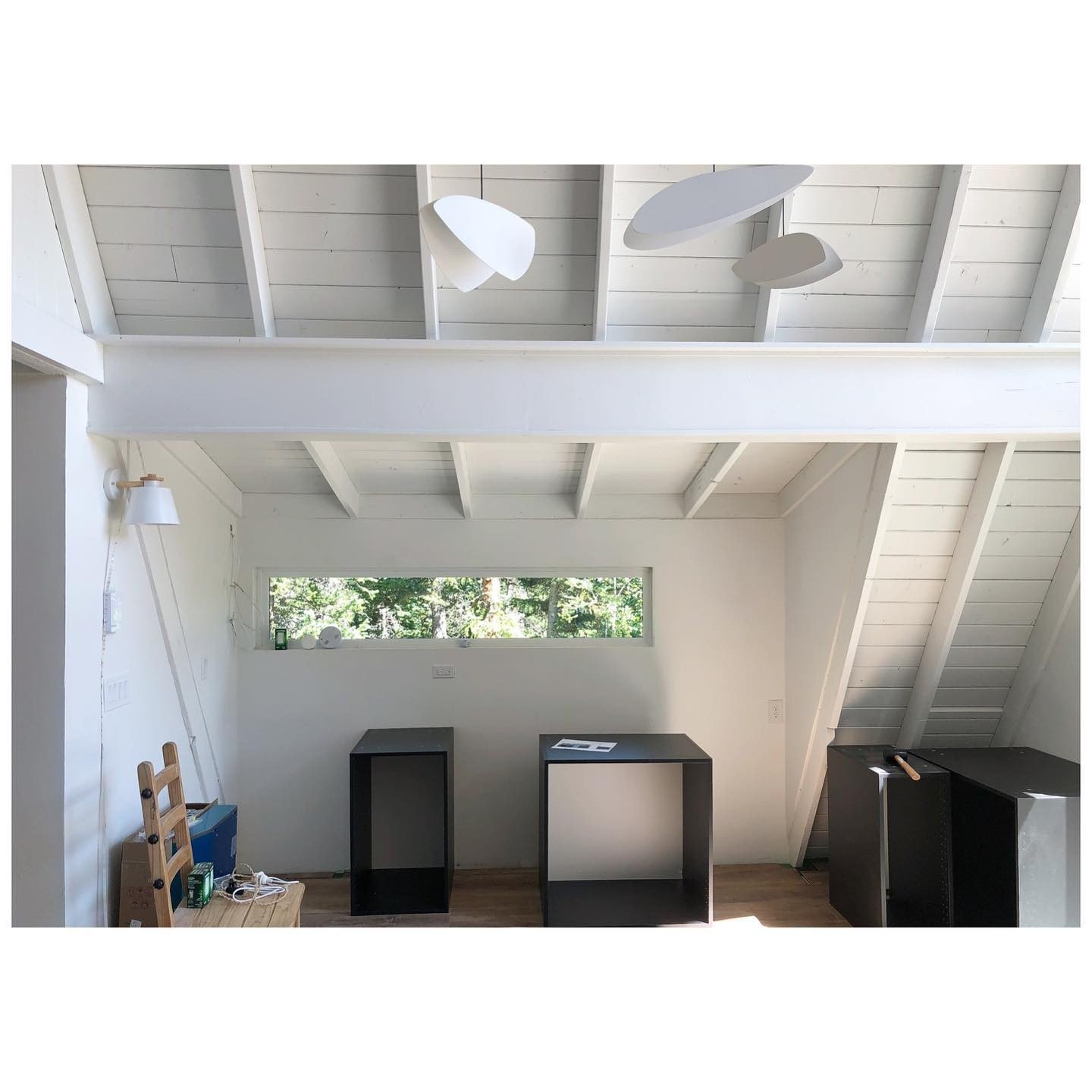 Cabin kitchen during renovation with a long horizontal window, white roof beams and appliances awaiting installation