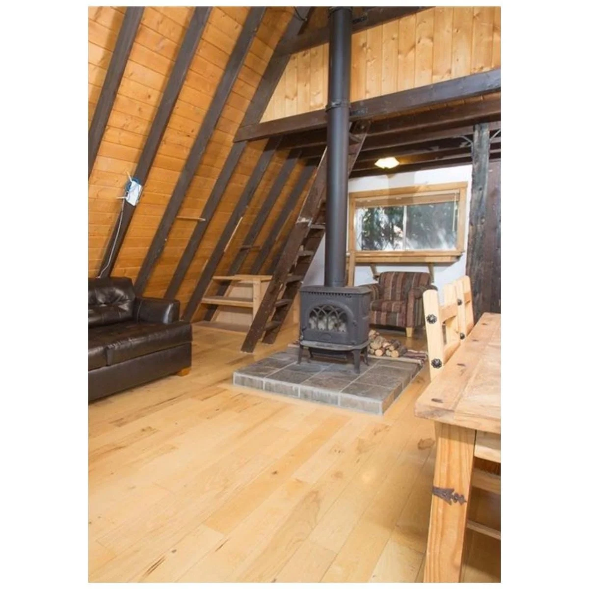 Cabin interior before renovation with exposed timber walls and roof beams around an older stove