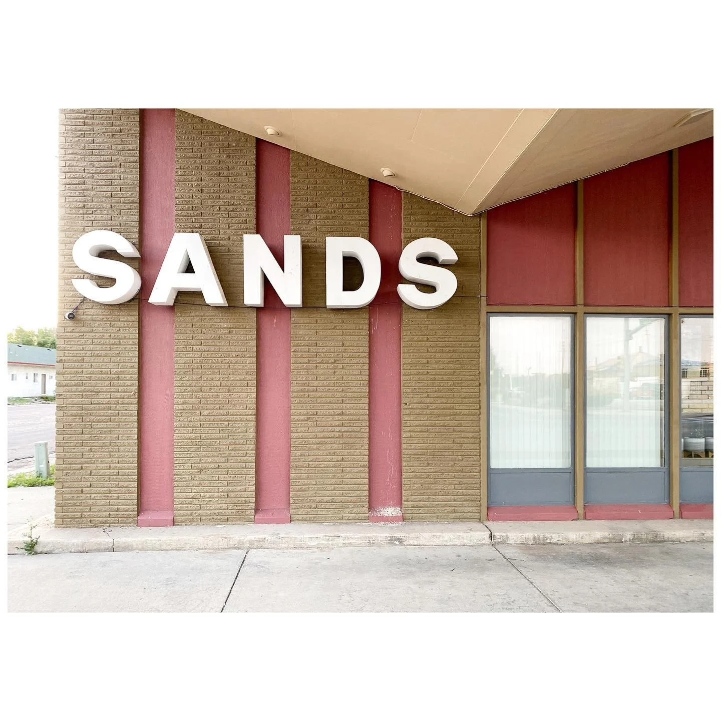 Sands lettering above a low motel facade with pink vertical accents