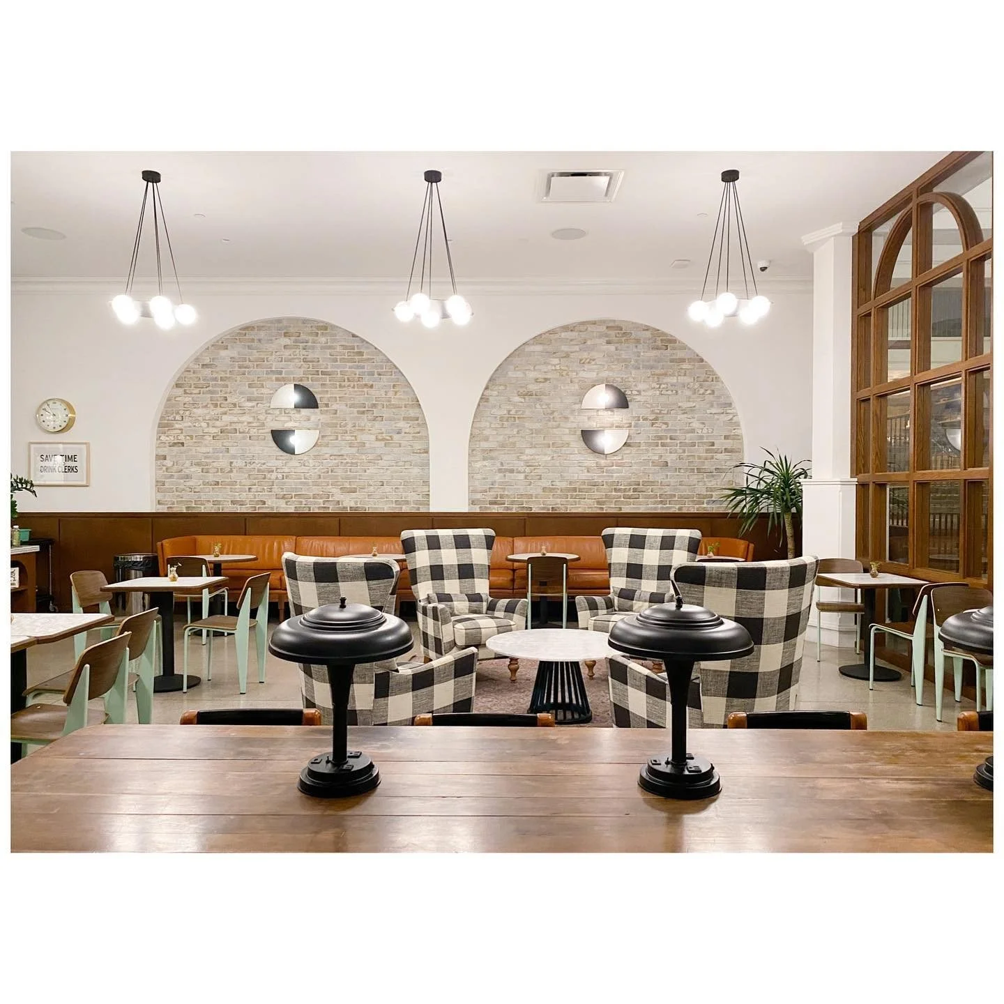 Cafe lounge with black-and-white buffalo plaid chairs, arched brick wall niches and pendant lights