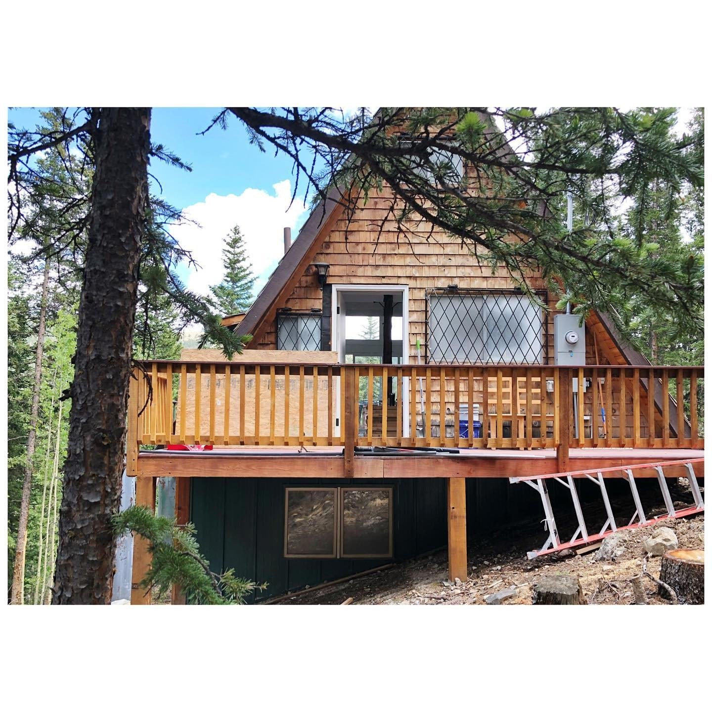 A-frame cabin with an older timber-shingled facade, pale door and timber deck during renovation
