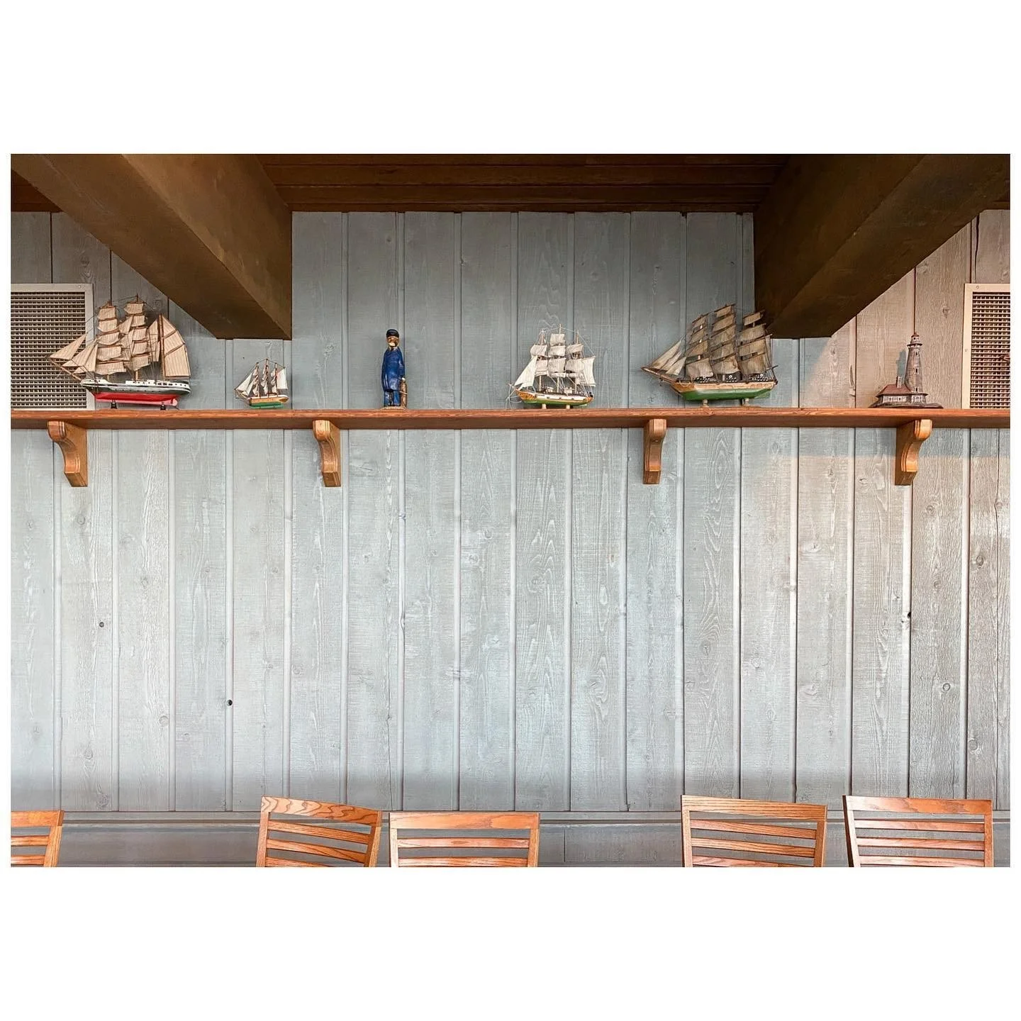 Model sailing ships arranged across a long timber shelf beneath exposed ceiling beams
