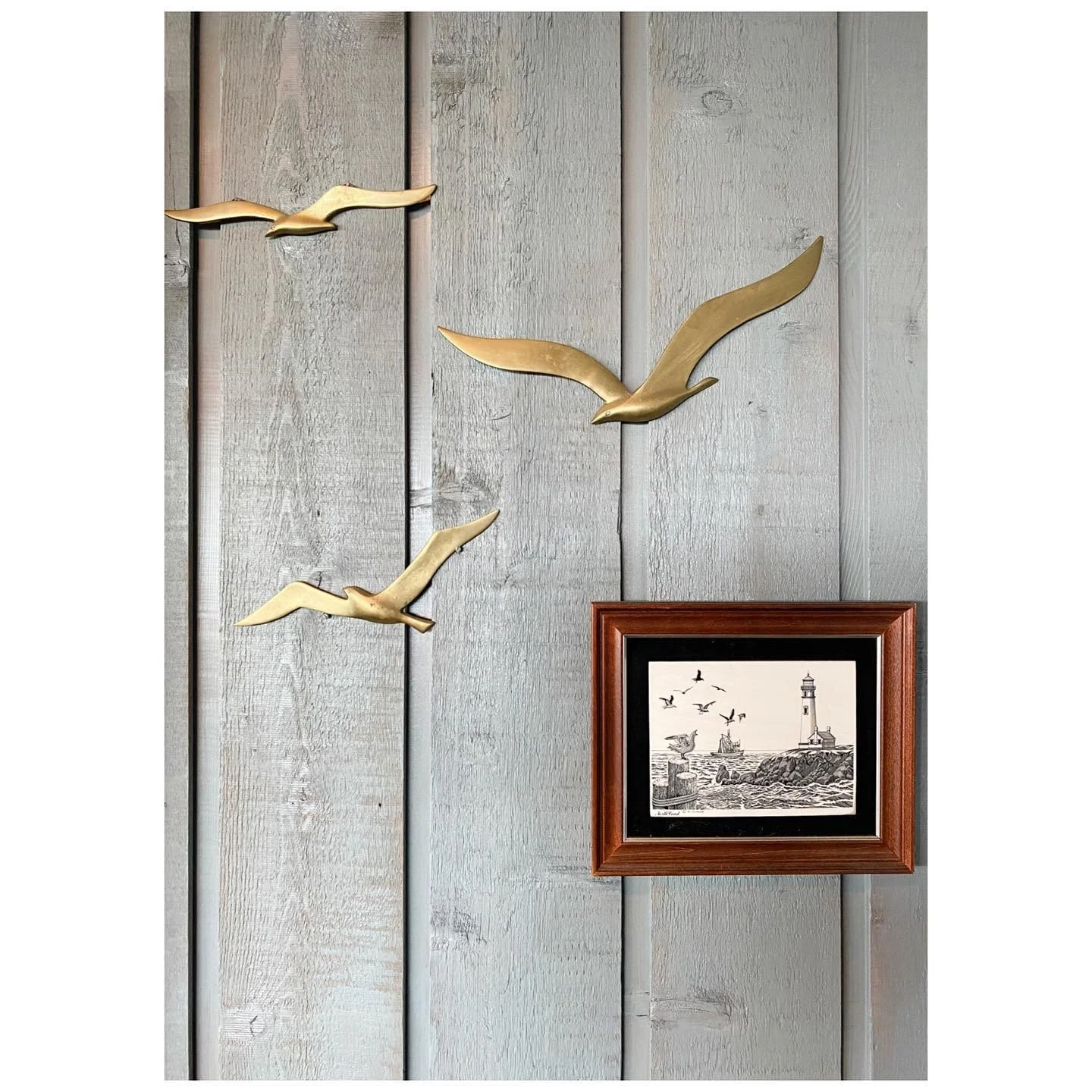 Brass bird ornaments and a small framed nautical print on a pale timber-paneled wall