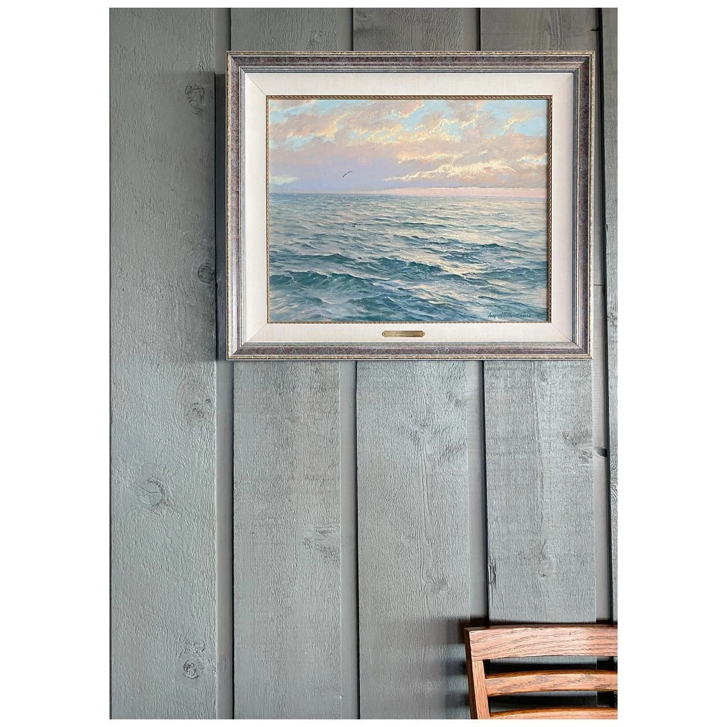 Small framed seascape against a pale blue timber-paneled wall