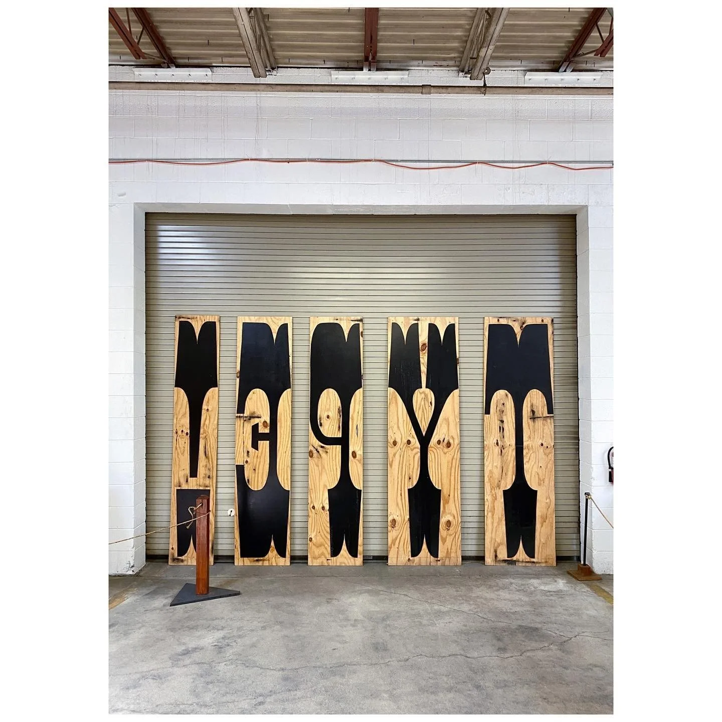 Oversized carved timber printing blocks arranged in front of a workshop roller door