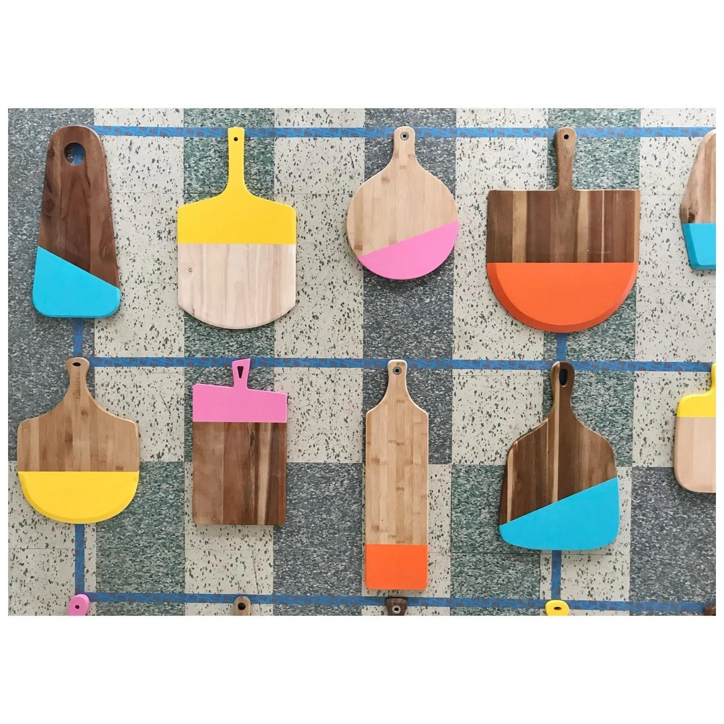Color-dipped cutting boards in yellow, turquoise, pink and orange arranged against a textured wall