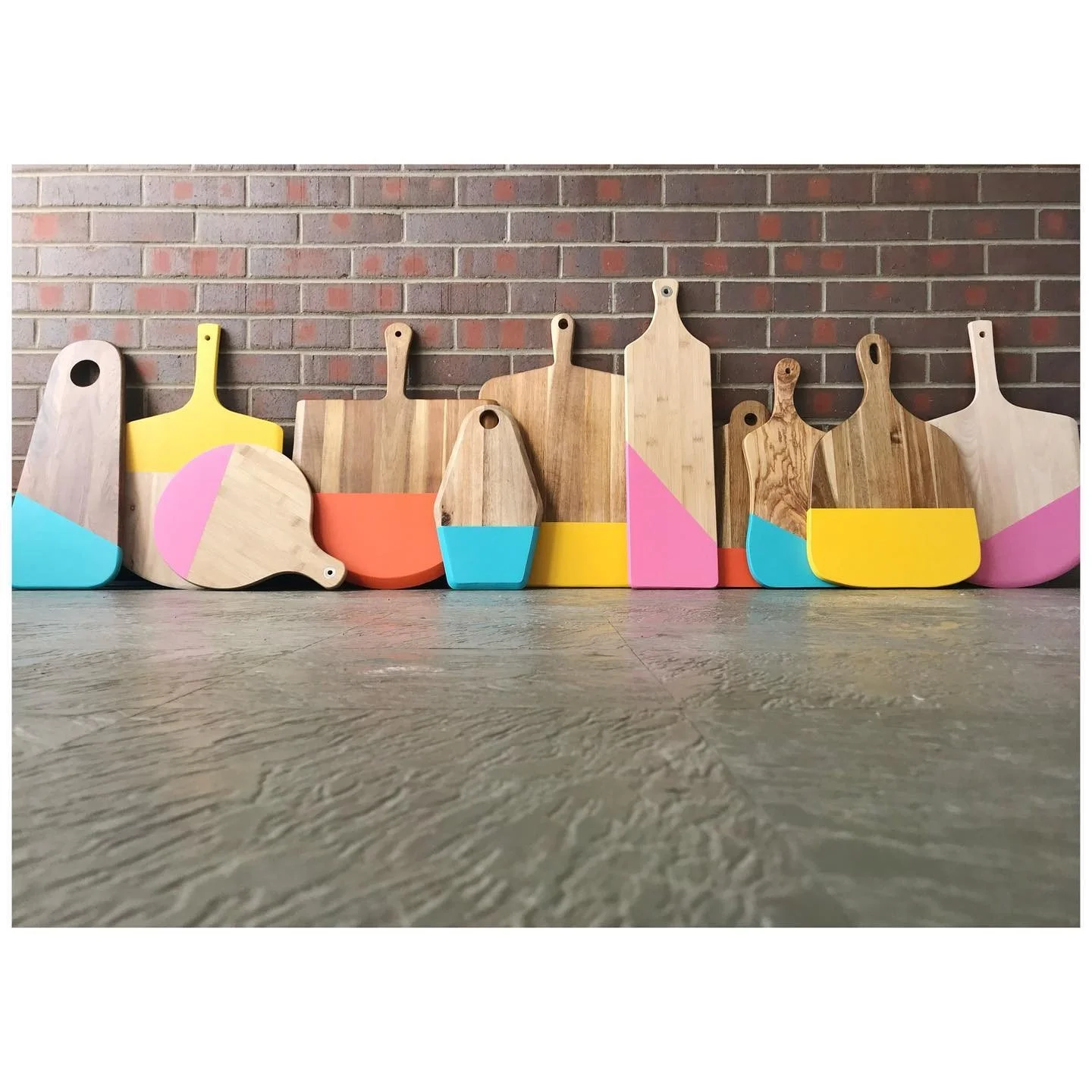 Brightly painted timber cutting boards lined up in front of an exposed brick wall