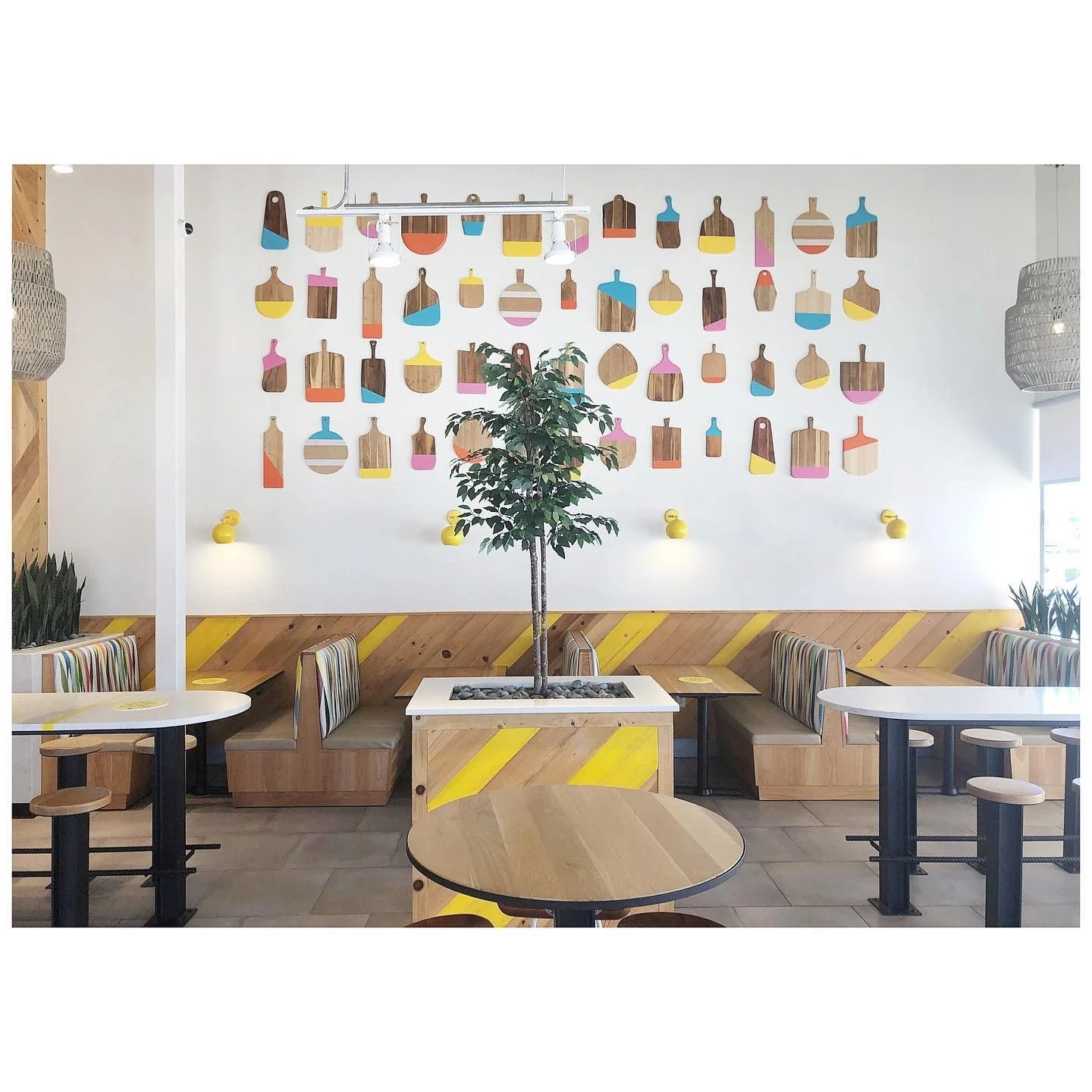 Restaurant dining space with a full wall of colorful cutting boards above timber seating