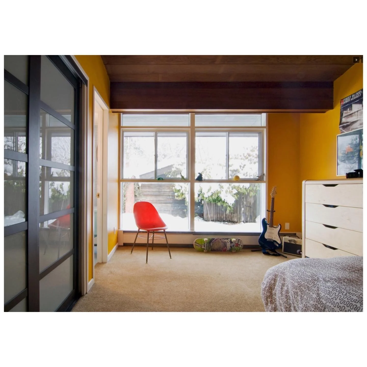 Earlier bedroom with yellow walls, timber ceiling beams, a red chair and broad windows
