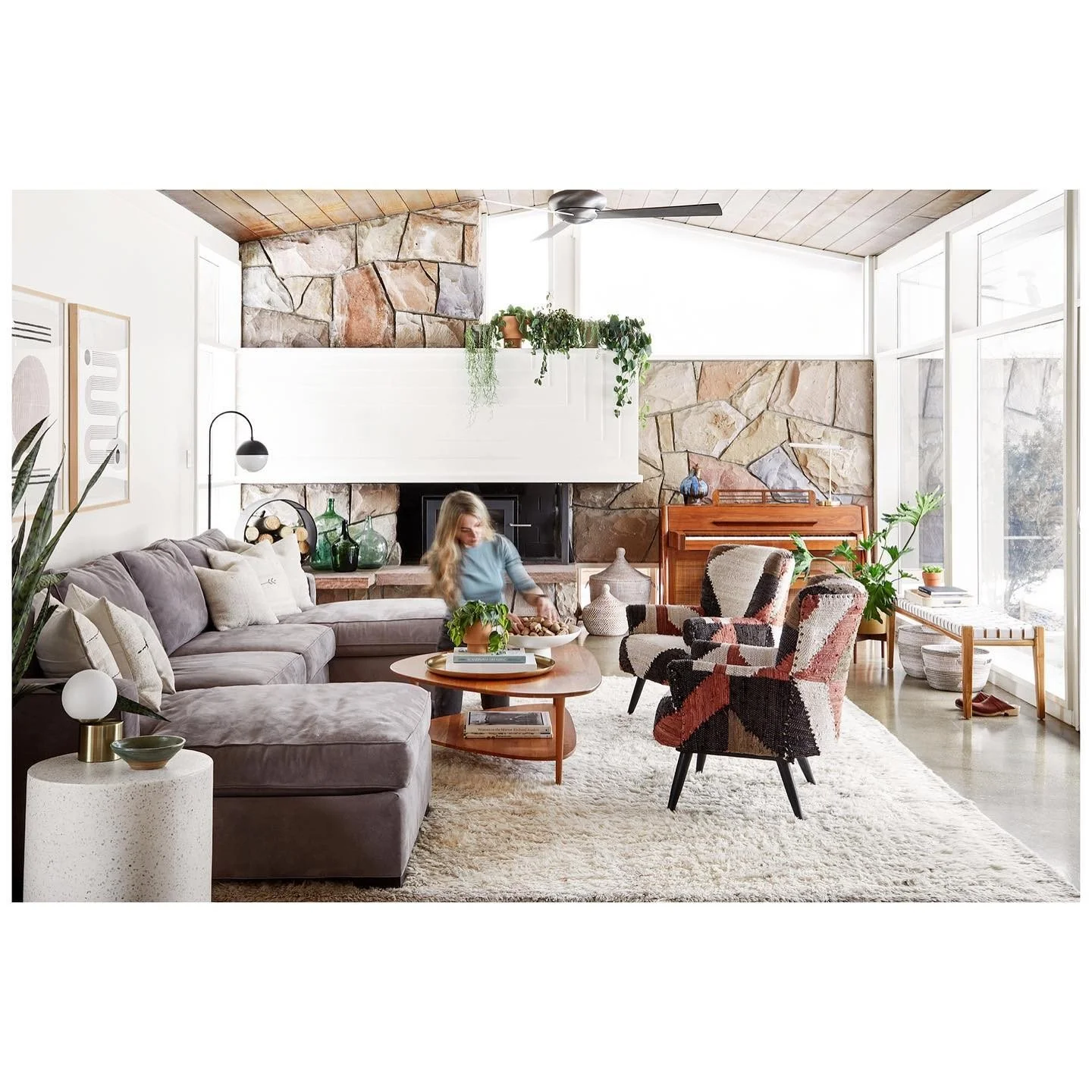 Designer adjusting a living room vignette with pale seating, layered rugs, plants and a large stone fireplace before photography