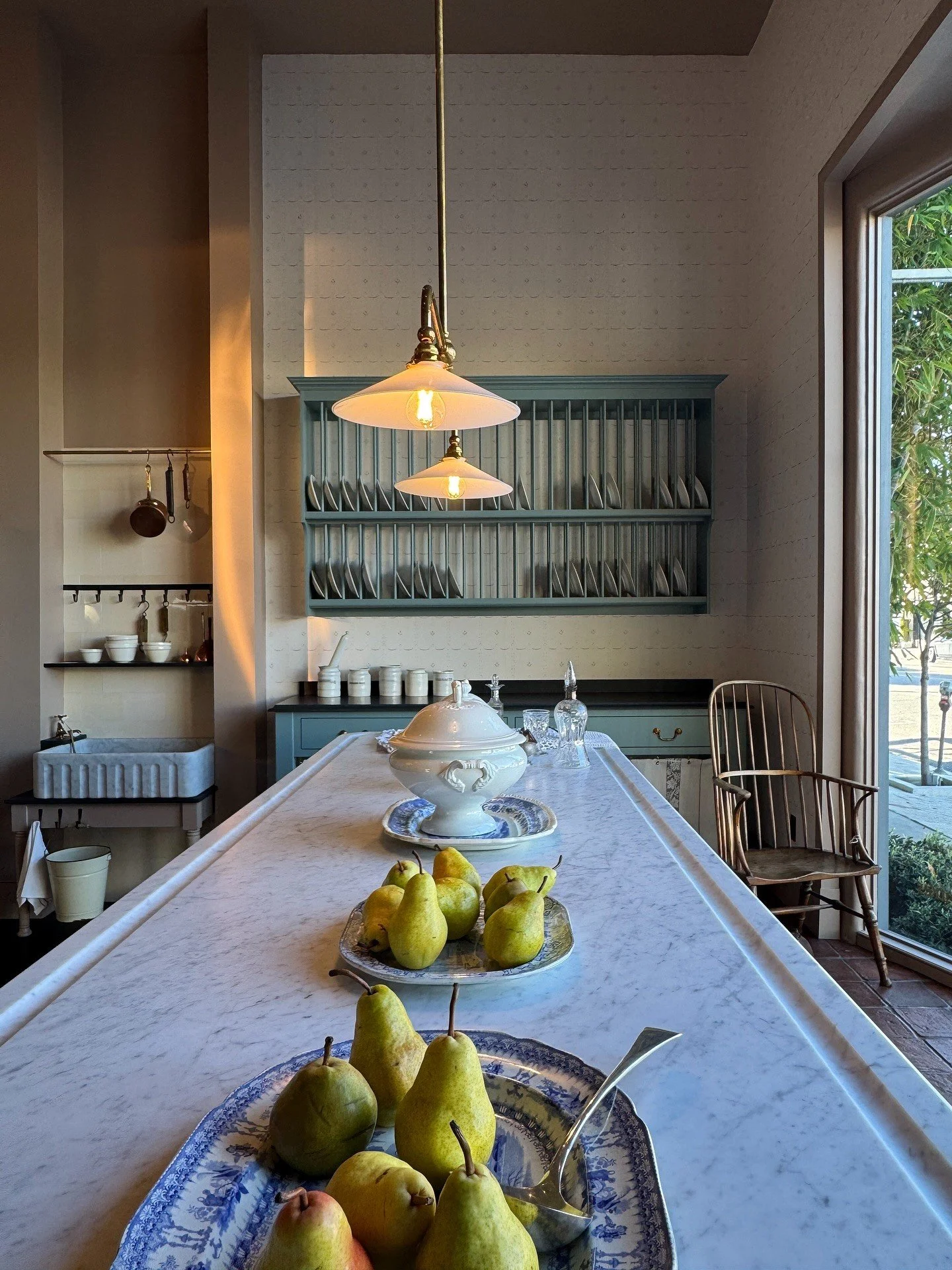 Long wood counter with bowls of pears beneath a brass pendant