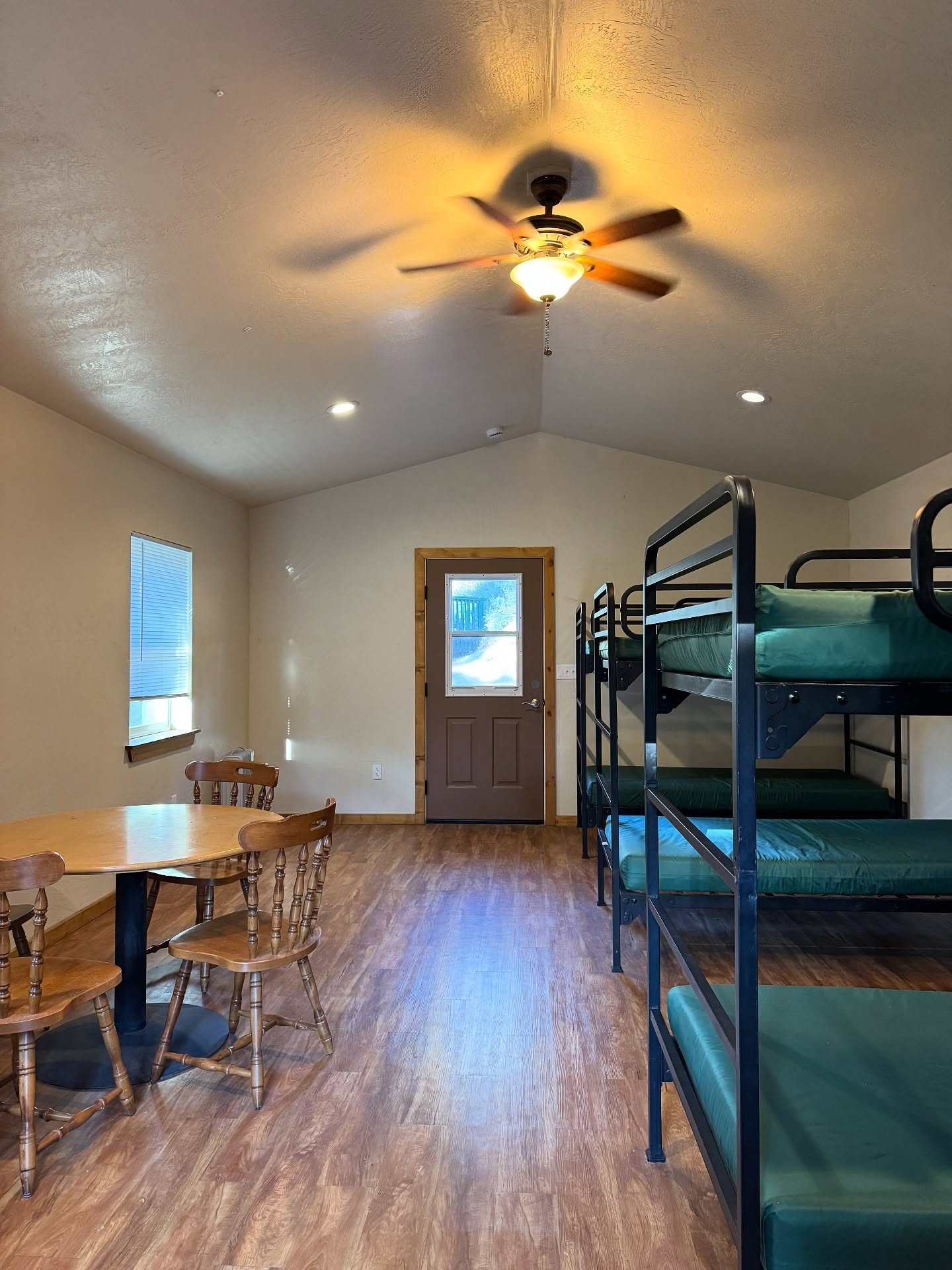 Simple timber-floored cabin with metal bunk beds and a ceiling fan