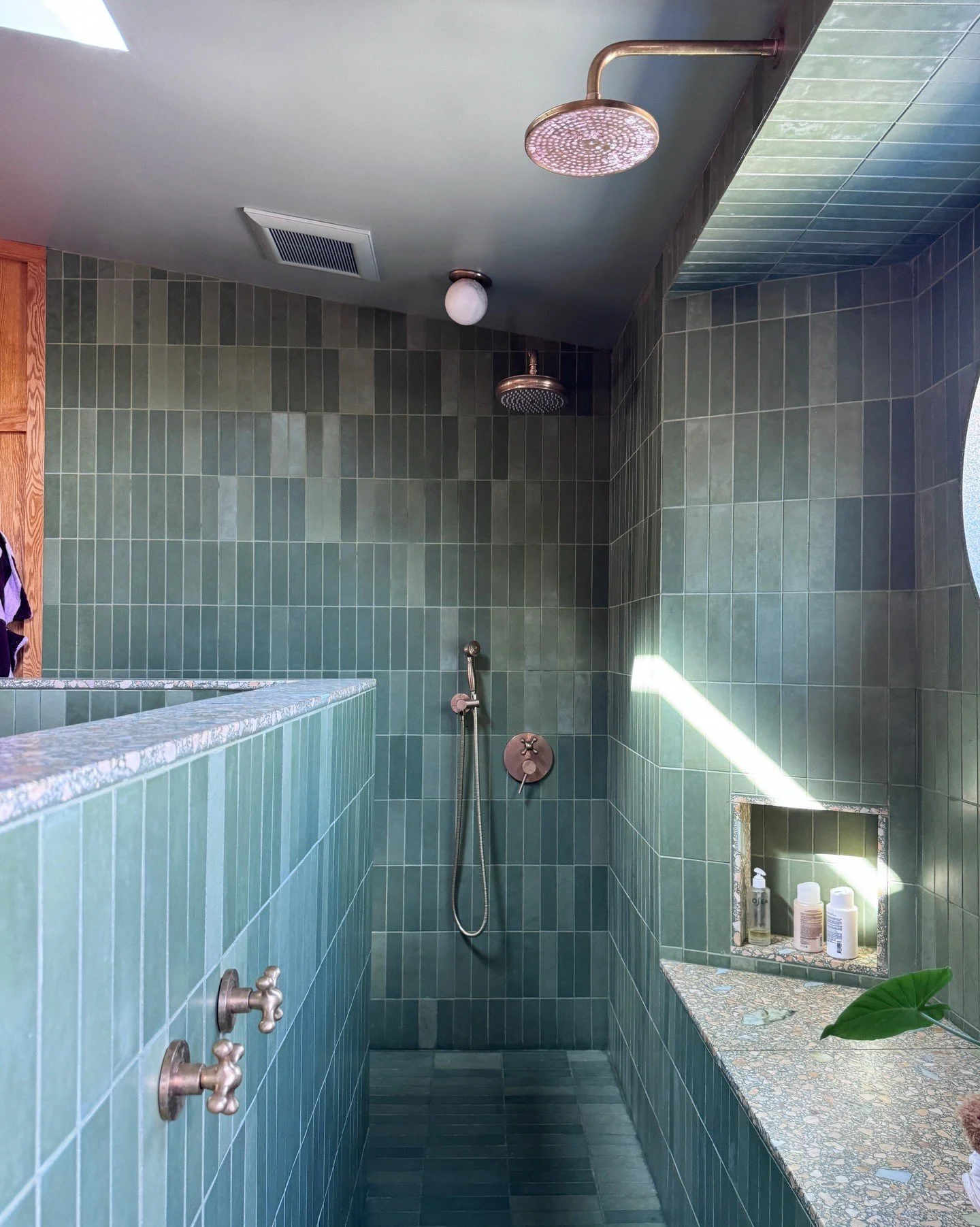 Green tile shower with terrazzo divider and pink showerhead